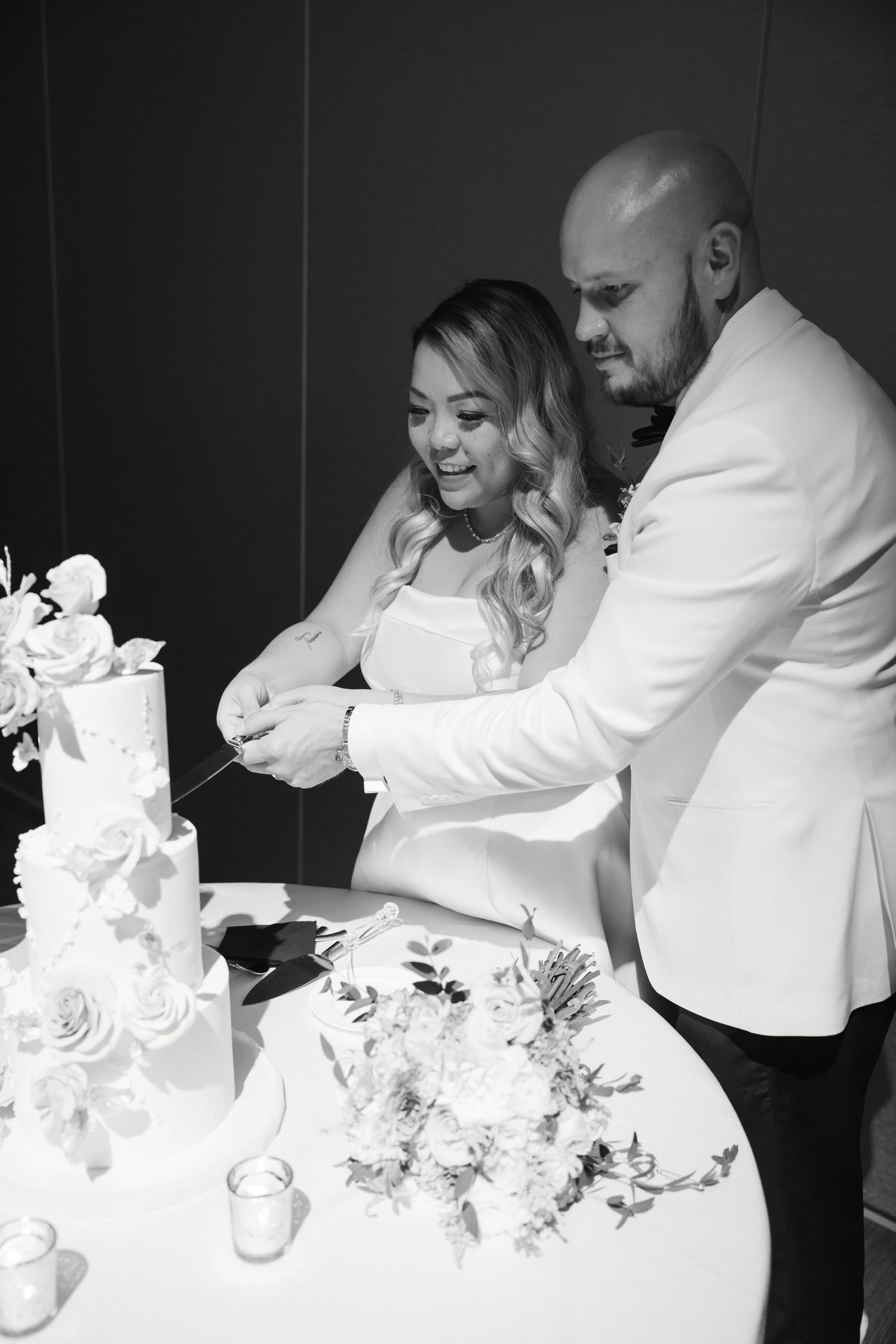 Black and white photo of couple cutting their elegant tiered wedding cake.