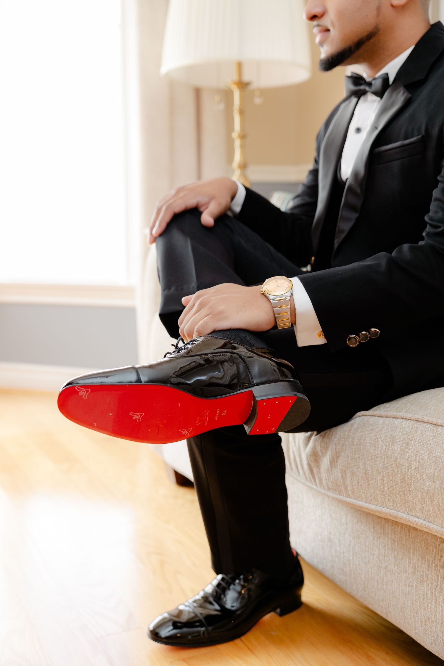Detail shot of formal black dress shoes with red soles on white couch.