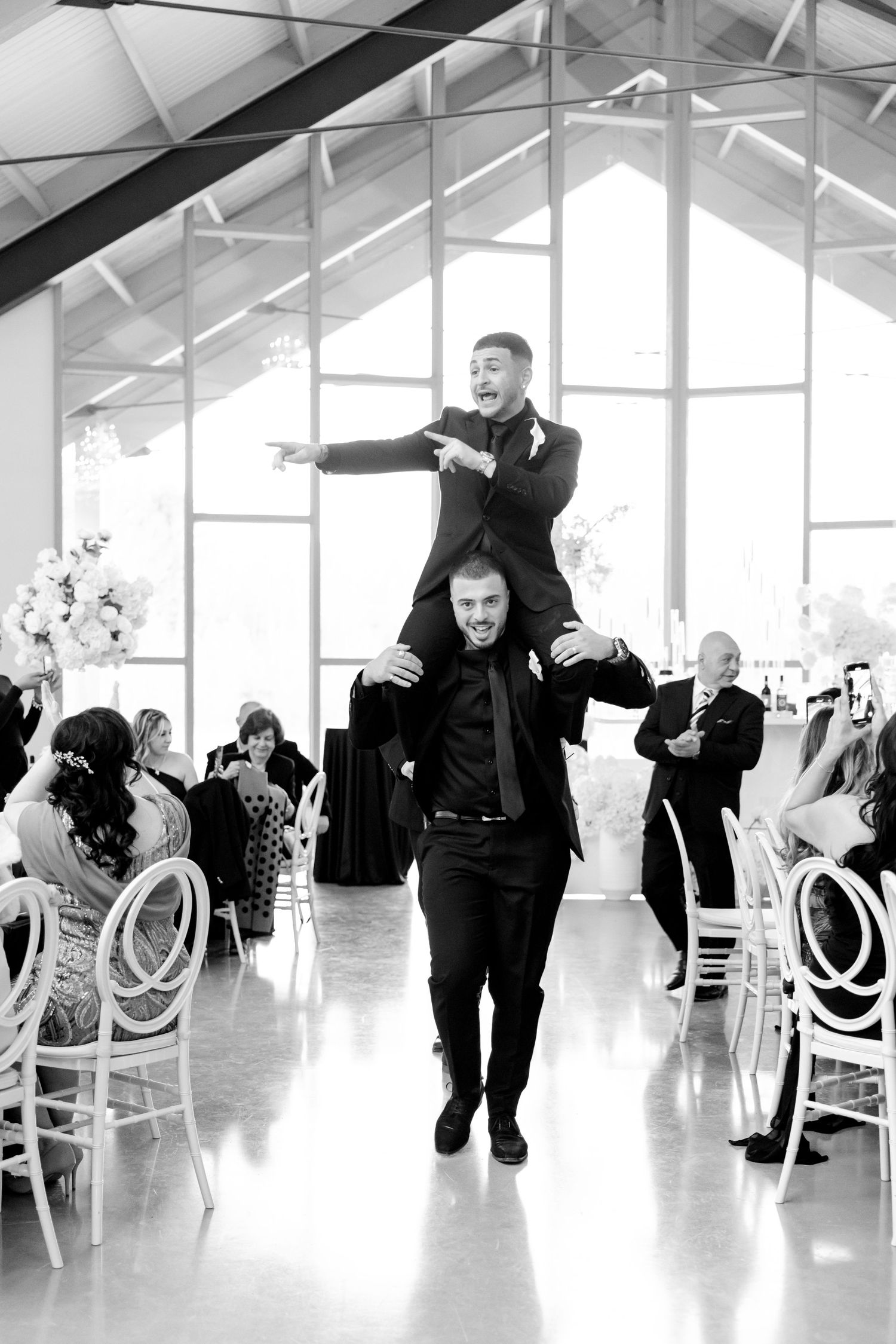 A playful moment during a wedding reception shows guests celebrating in a bright venue with high glass windows.