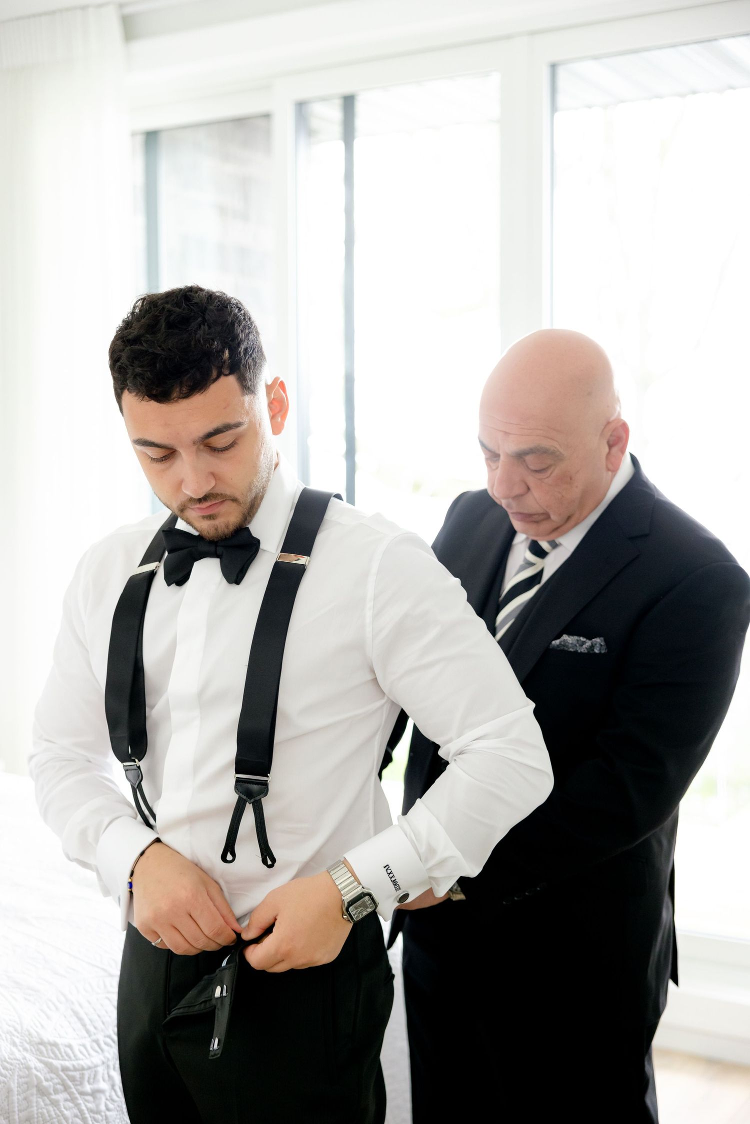 Getting ready scene with black suspenders being adjusted in bright room.