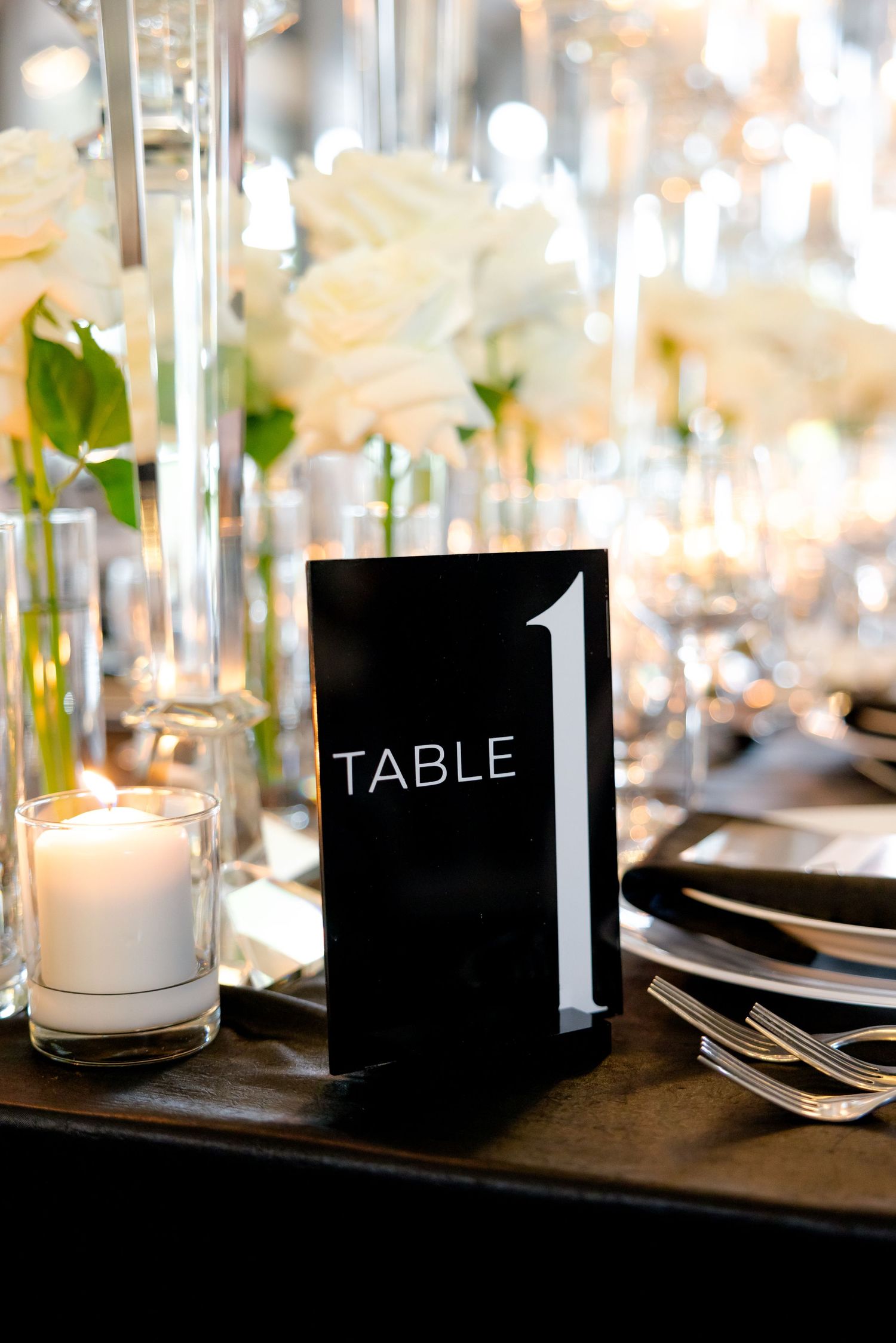 Modern black table number display with elegant place settings and white roses.