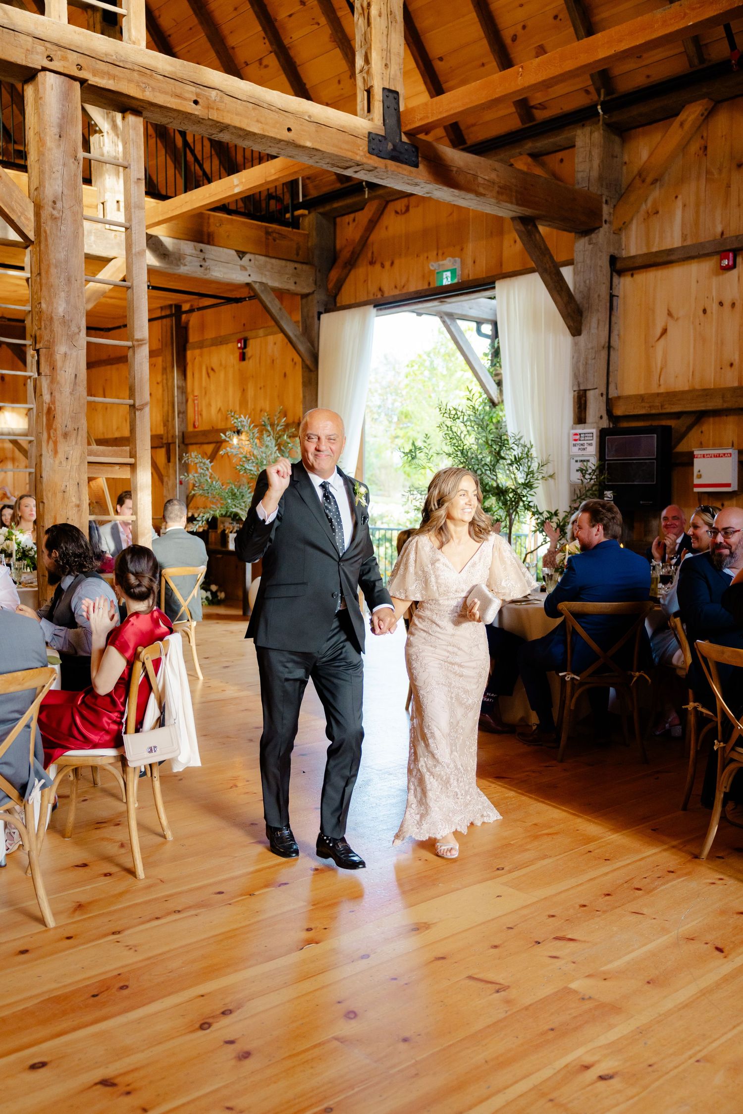 Wedding guests celebrate on a rustic wooden dance floor in a beautifully decorated barn.