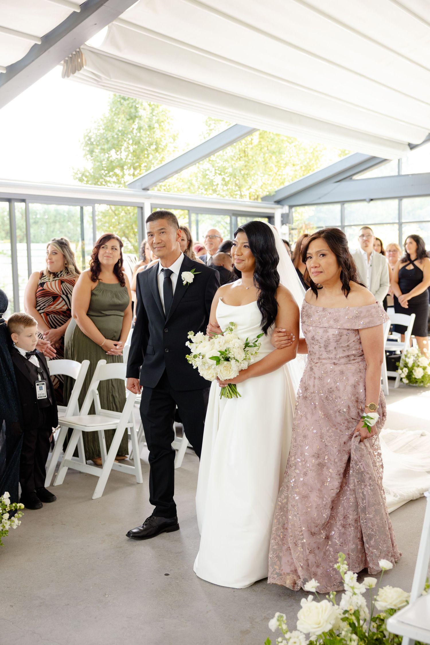 Wedding party stands together in a modern venue with white chairs and floral arrangements.