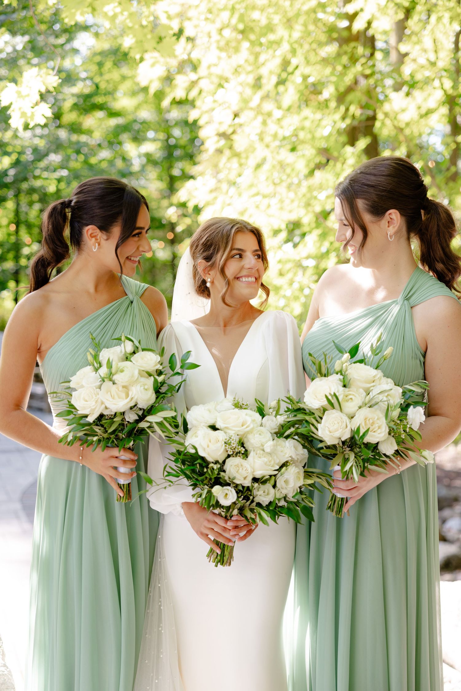 Bridal party in mint green dresses share happy moment while holding white floral bouquets.