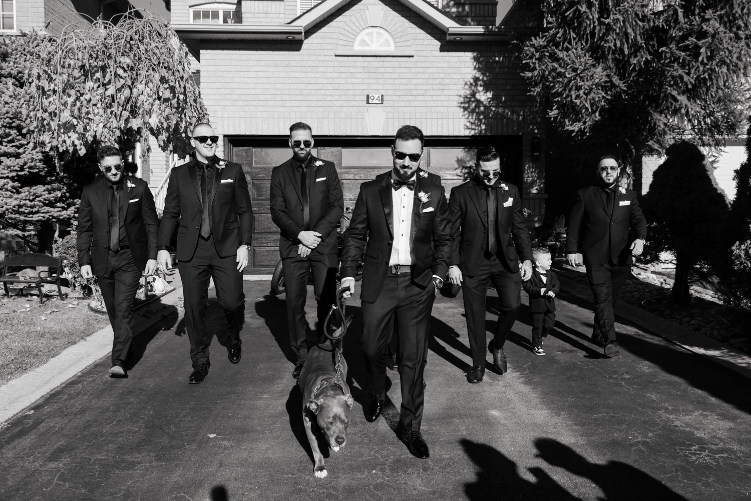 A black and white photo of people walking with a dog on a residential driveway.