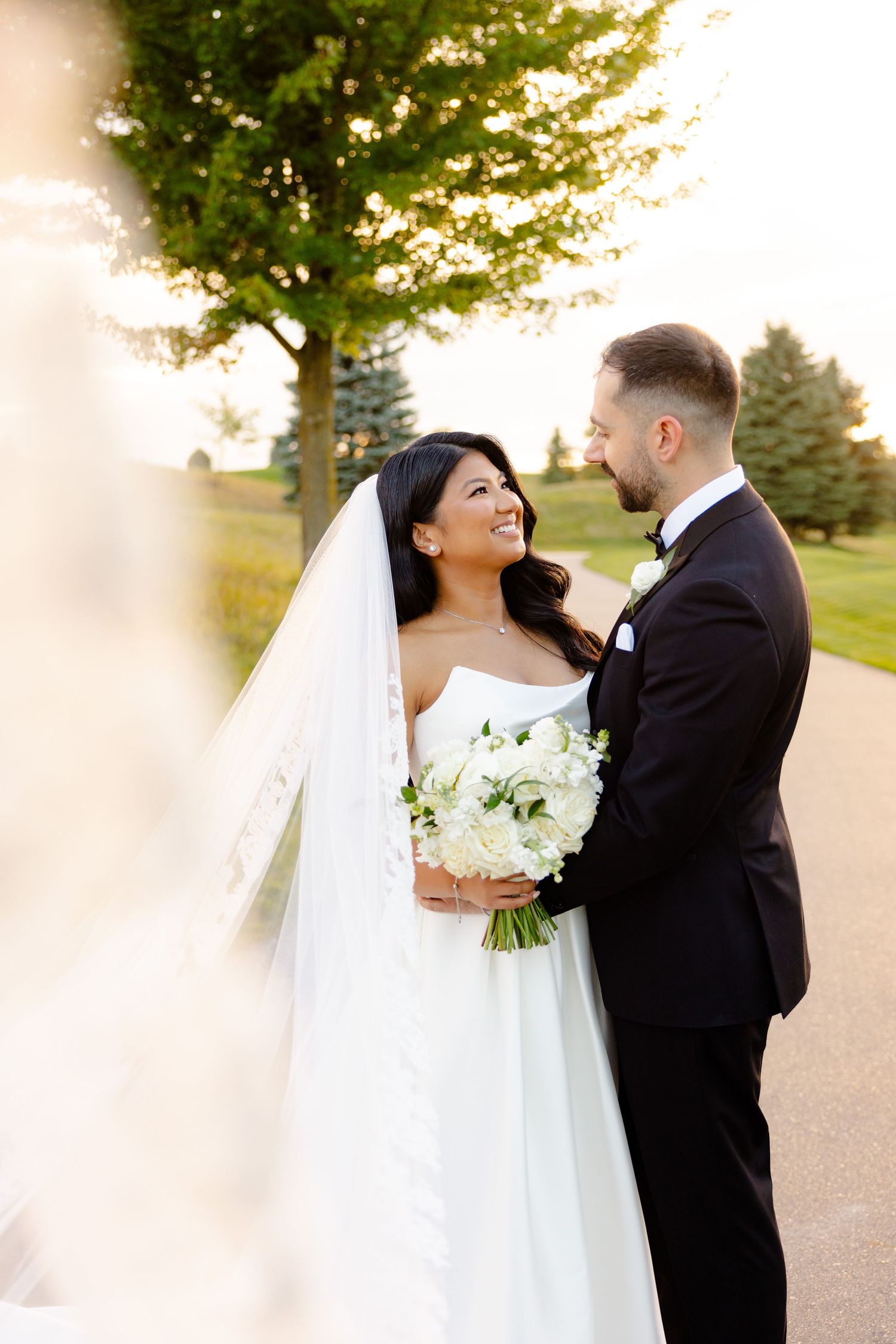 A tender wedding moment captured between newlyweds with soft golden lighting and trees in background.