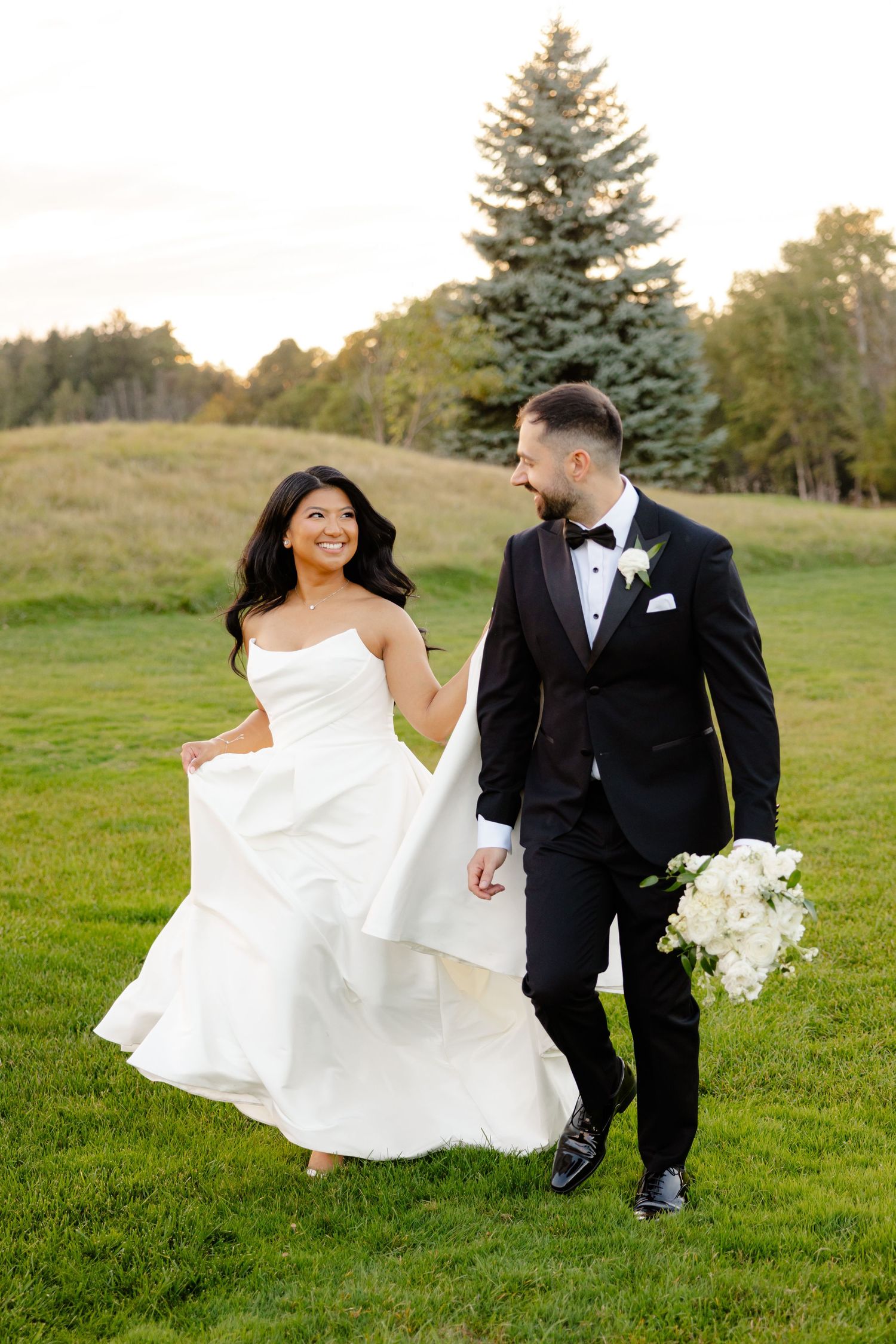 Elegant couple strolling through garden grounds with white dress flowing in the wind.