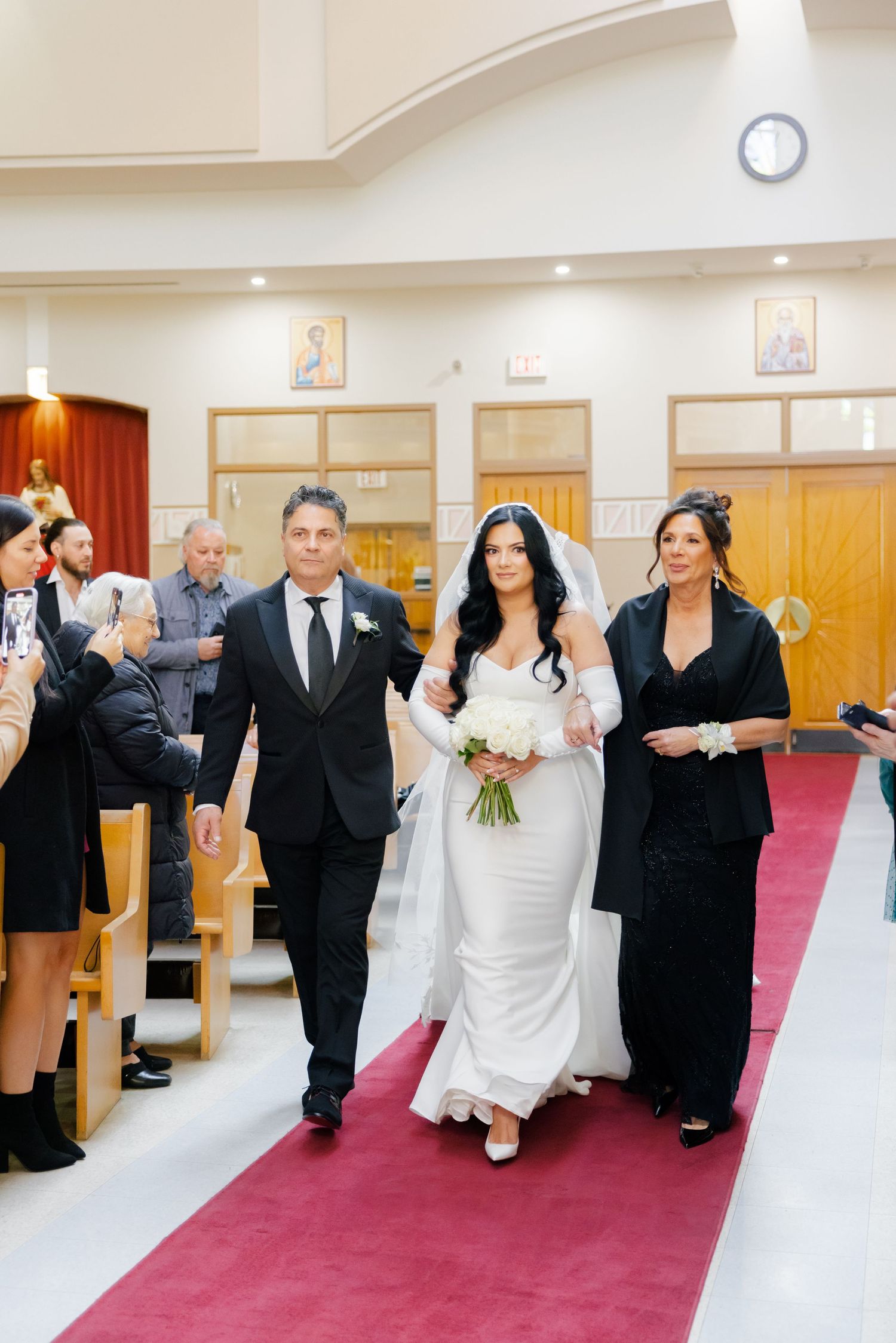 A wedding ceremony processional moves through a church with wooden pews and religious icons.