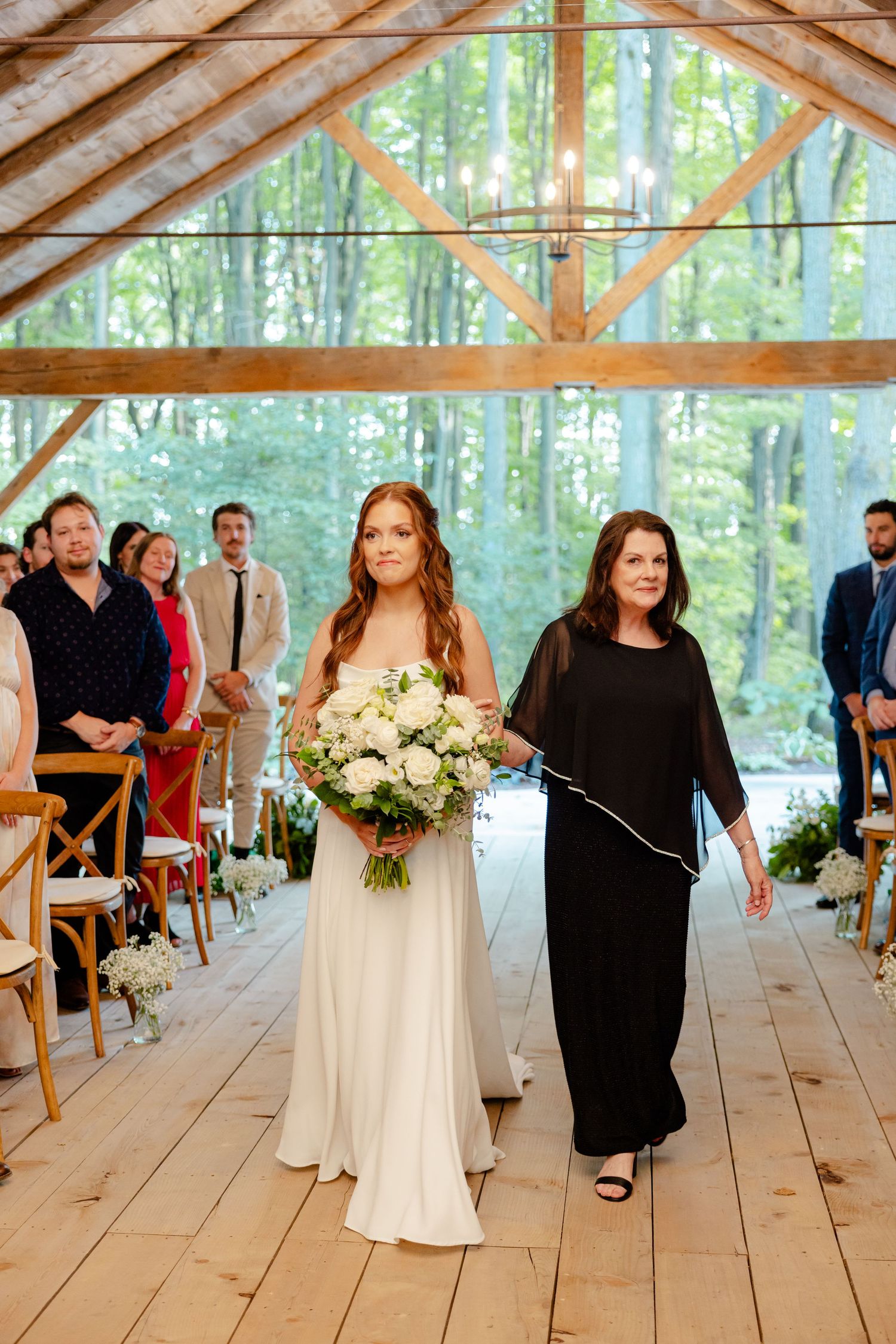 Wedding ceremony in a timber-frame pavilion with woodland backdrop as attendees look on.