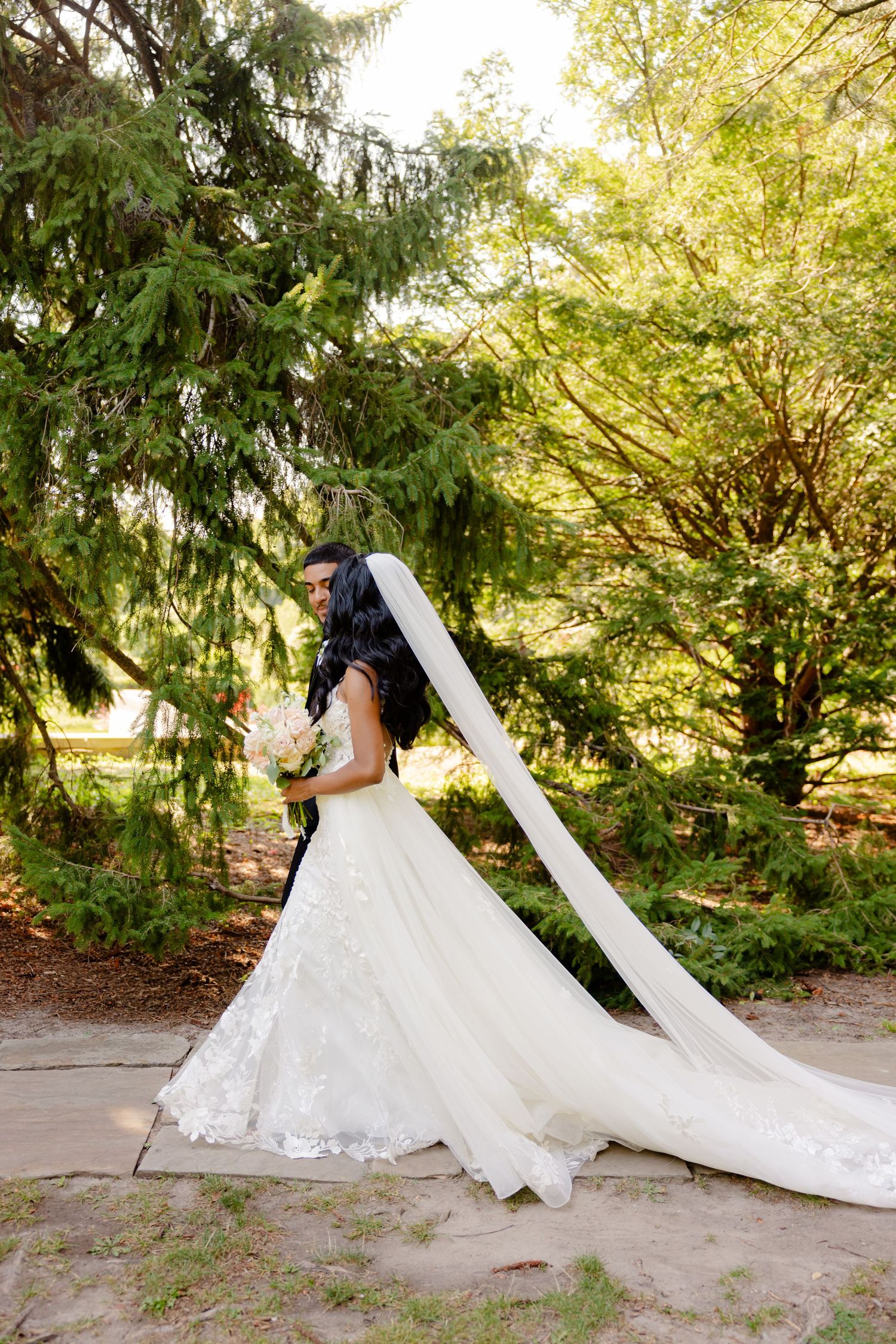 A stunning wedding dress with a dramatic cathedral-length veil photographed in a lush garden setting.