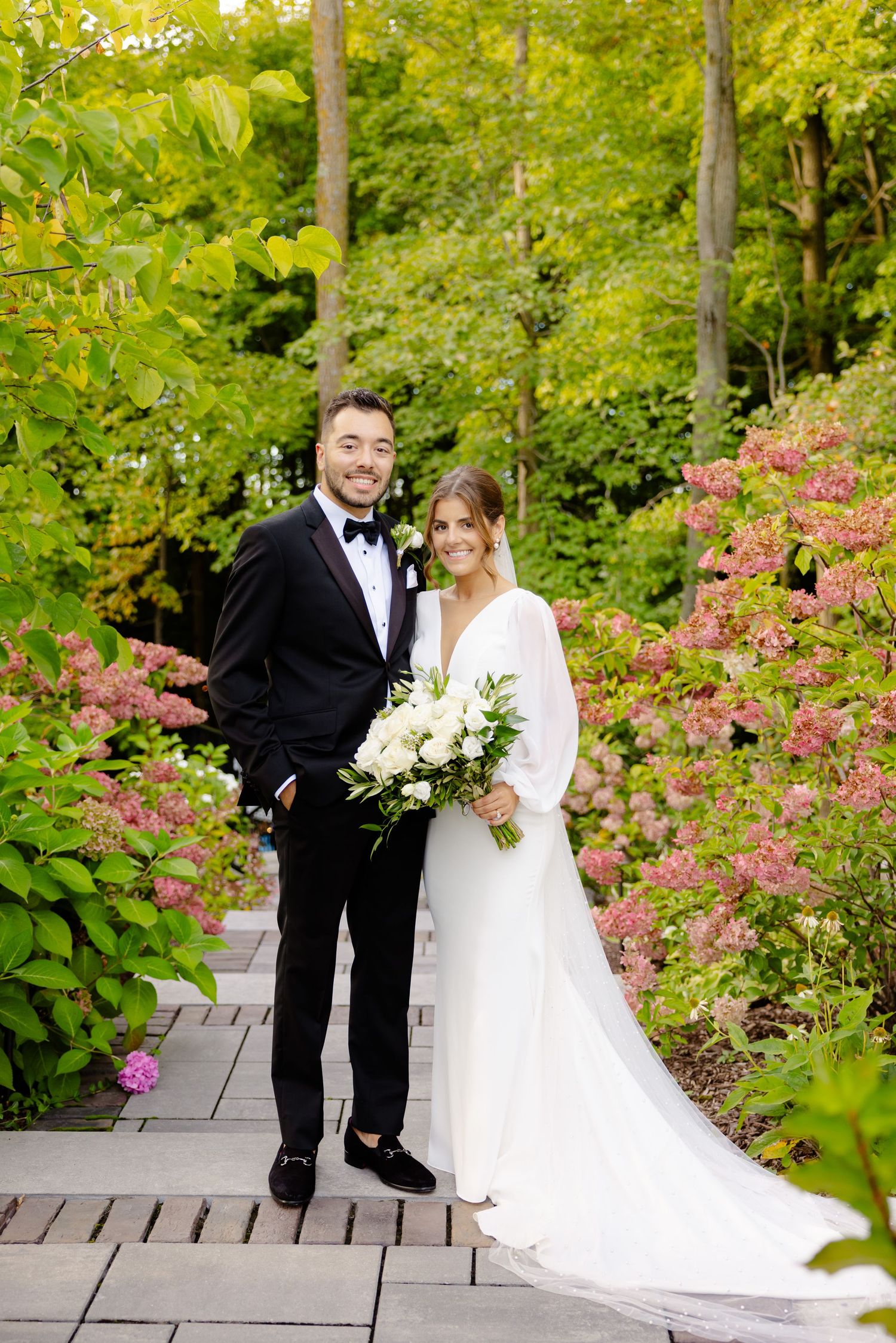 Garden wedding portrait featuring couple on wooden pathway with pink flowers and green foliage.