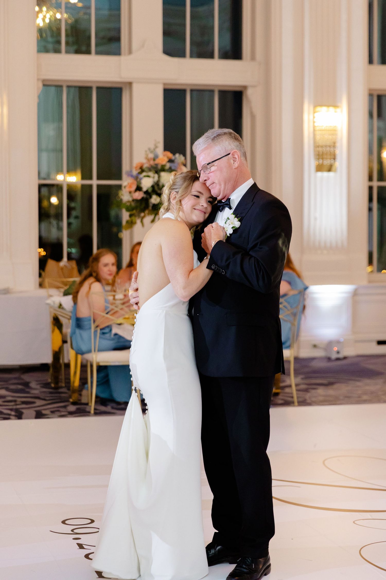Intimate first dance moment in an elegant white ballroom with large windows and romantic lighting.
