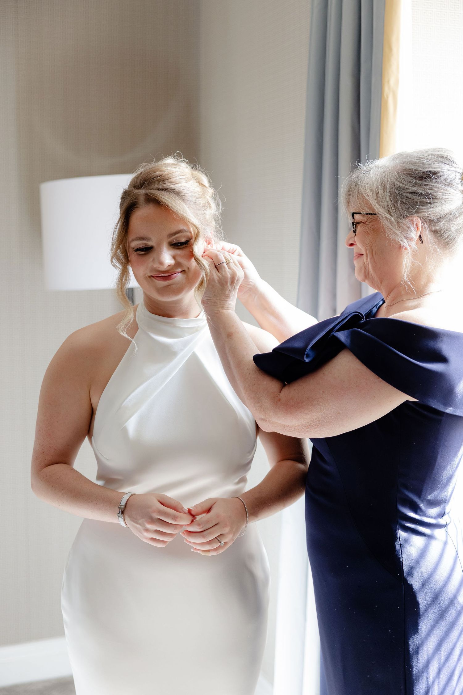 A series of photos showing someone being helped into a white wedding dress in a bright sunlit room.