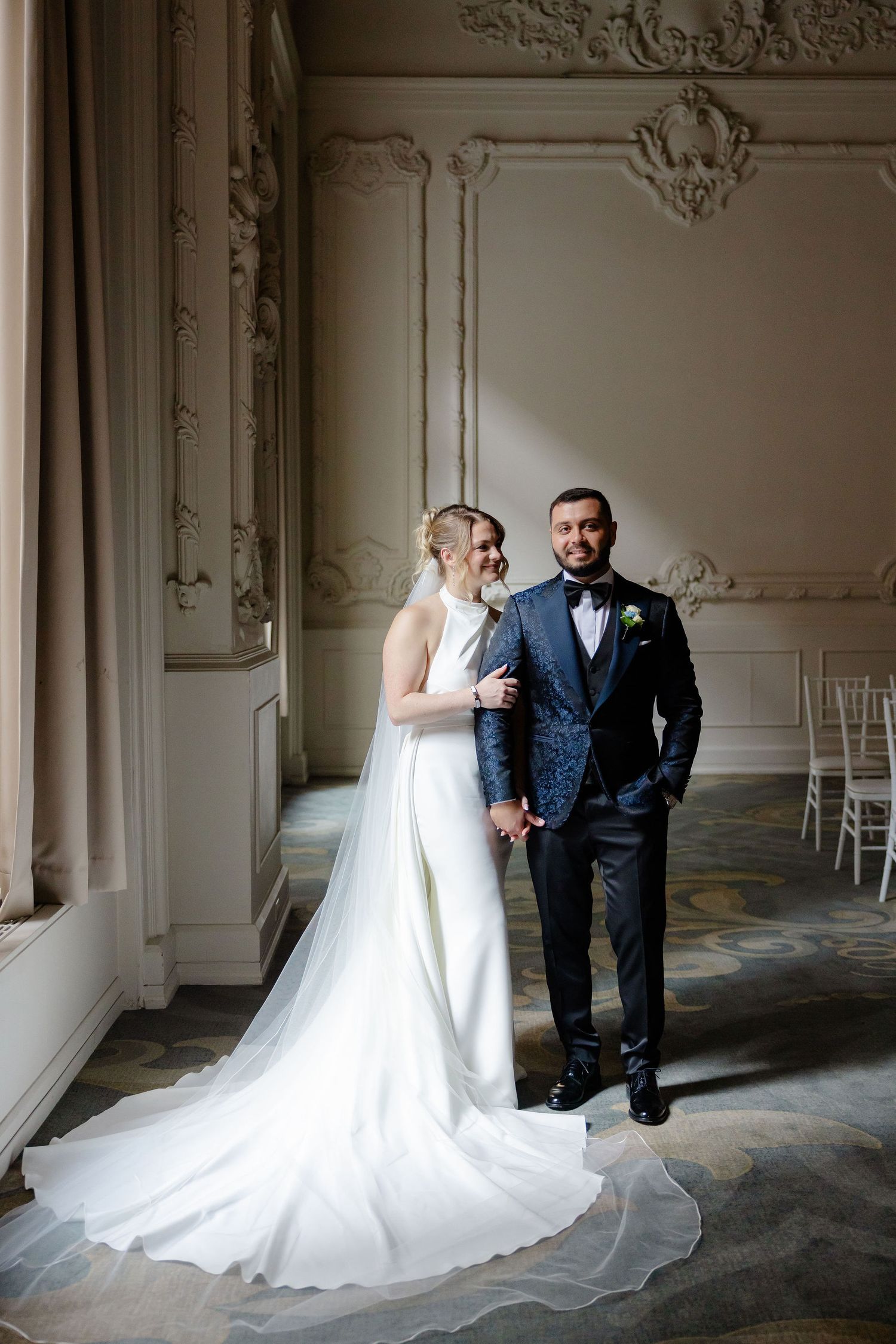 Wedding couple posing in elegant room with dramatic lighting and flowing white dress train.
