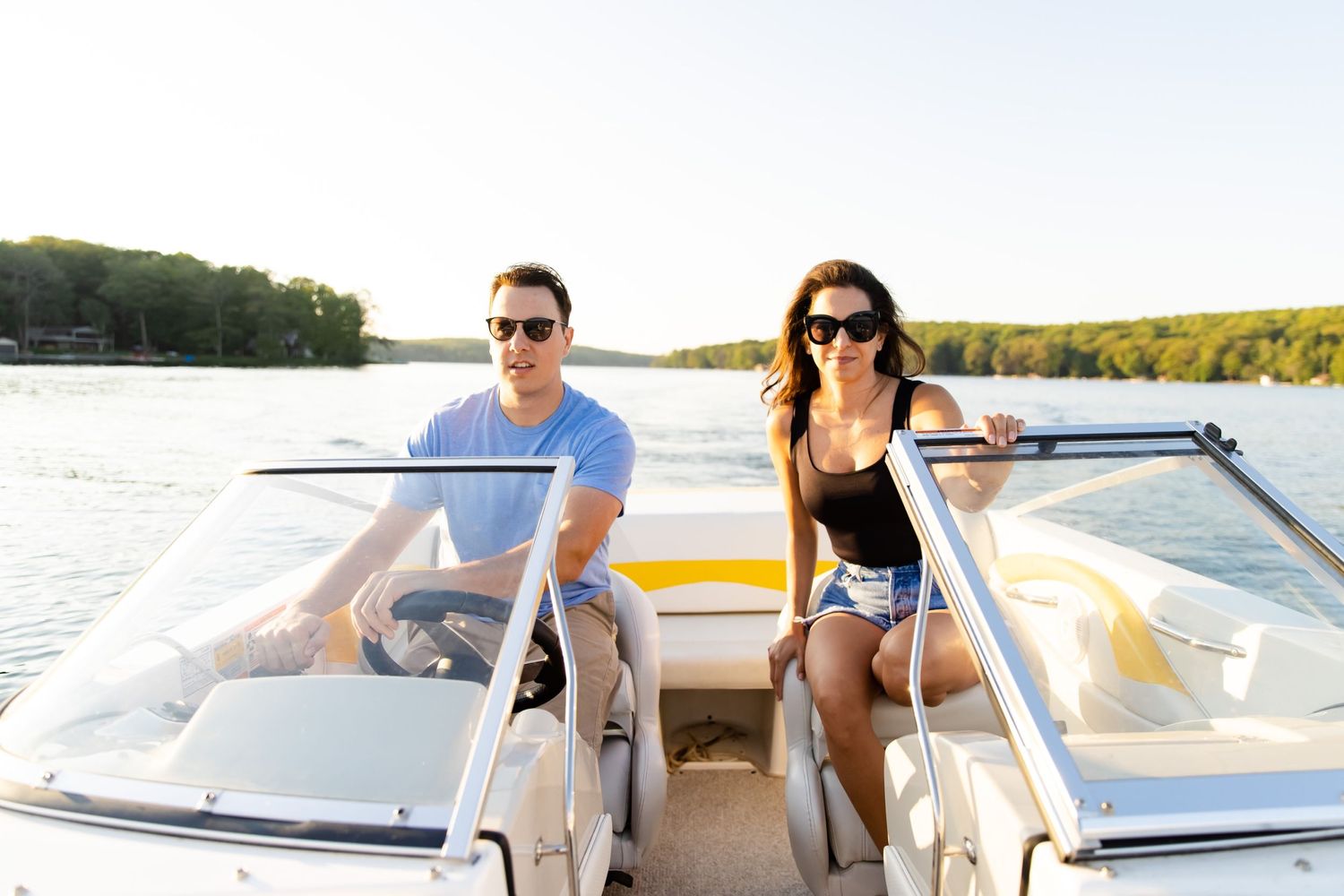 Couple sitting in boat wearing sunglasses during summer lake day.