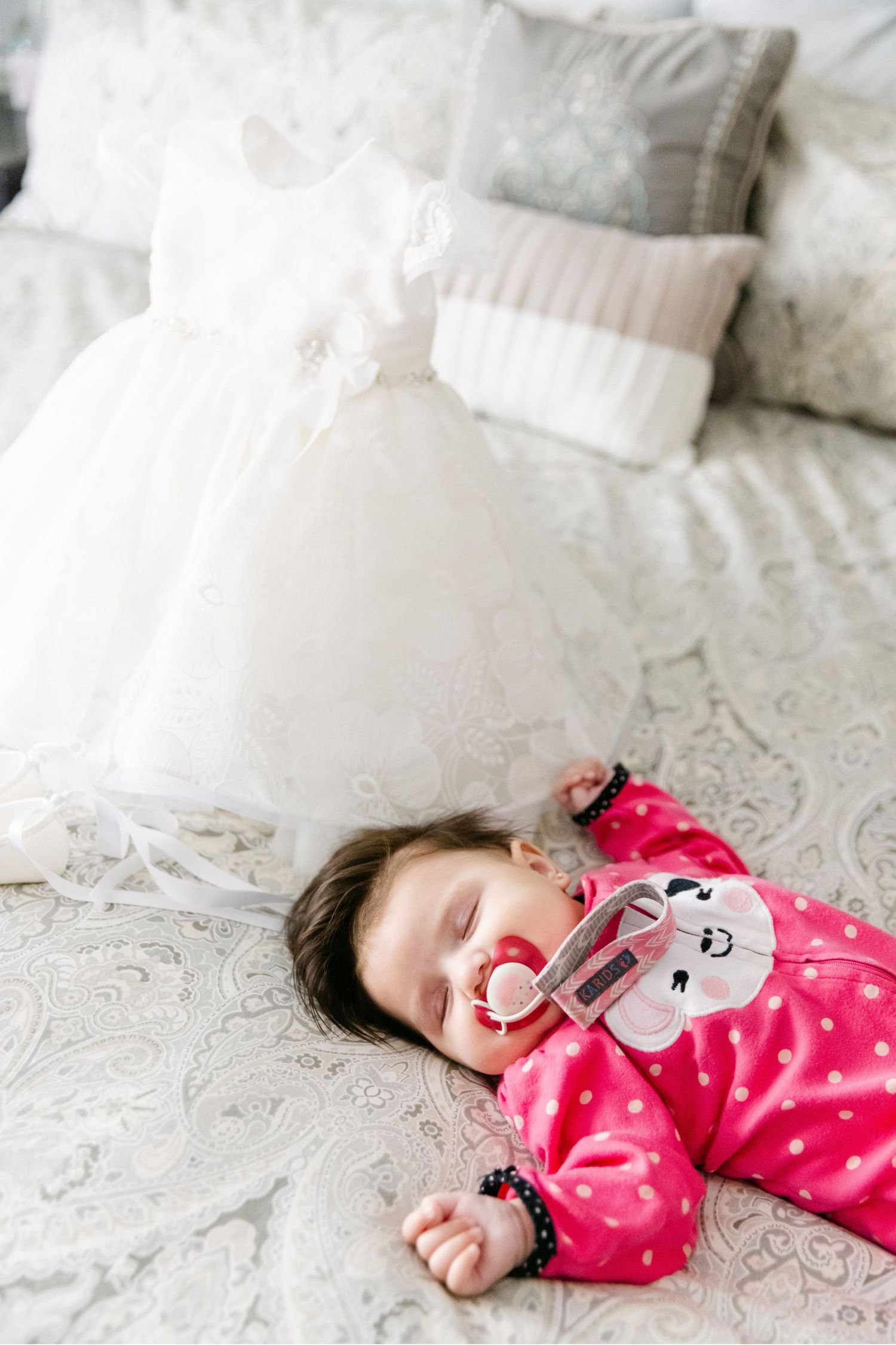Small baby sleeping peacefully on white bedding while wearing pink polka dot pajamas.