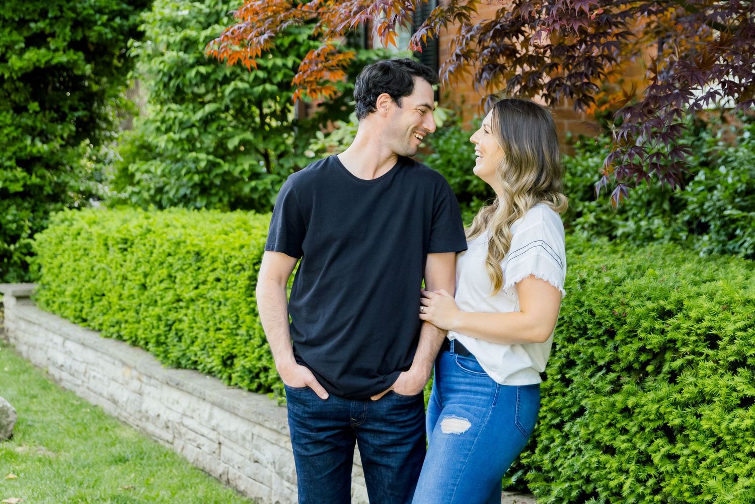 A couple sharing a casual moment together by a manicured garden hedge.