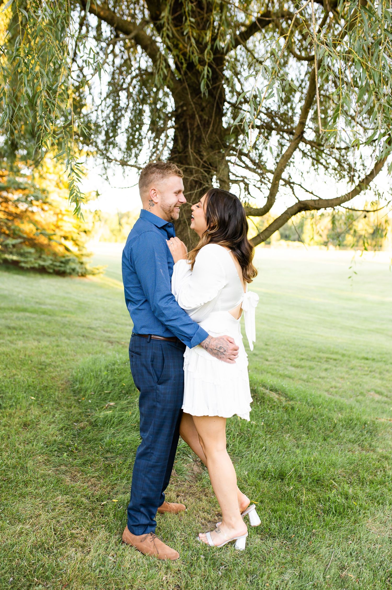 A couple embraces under a weeping willow tree in a serene garden setting.