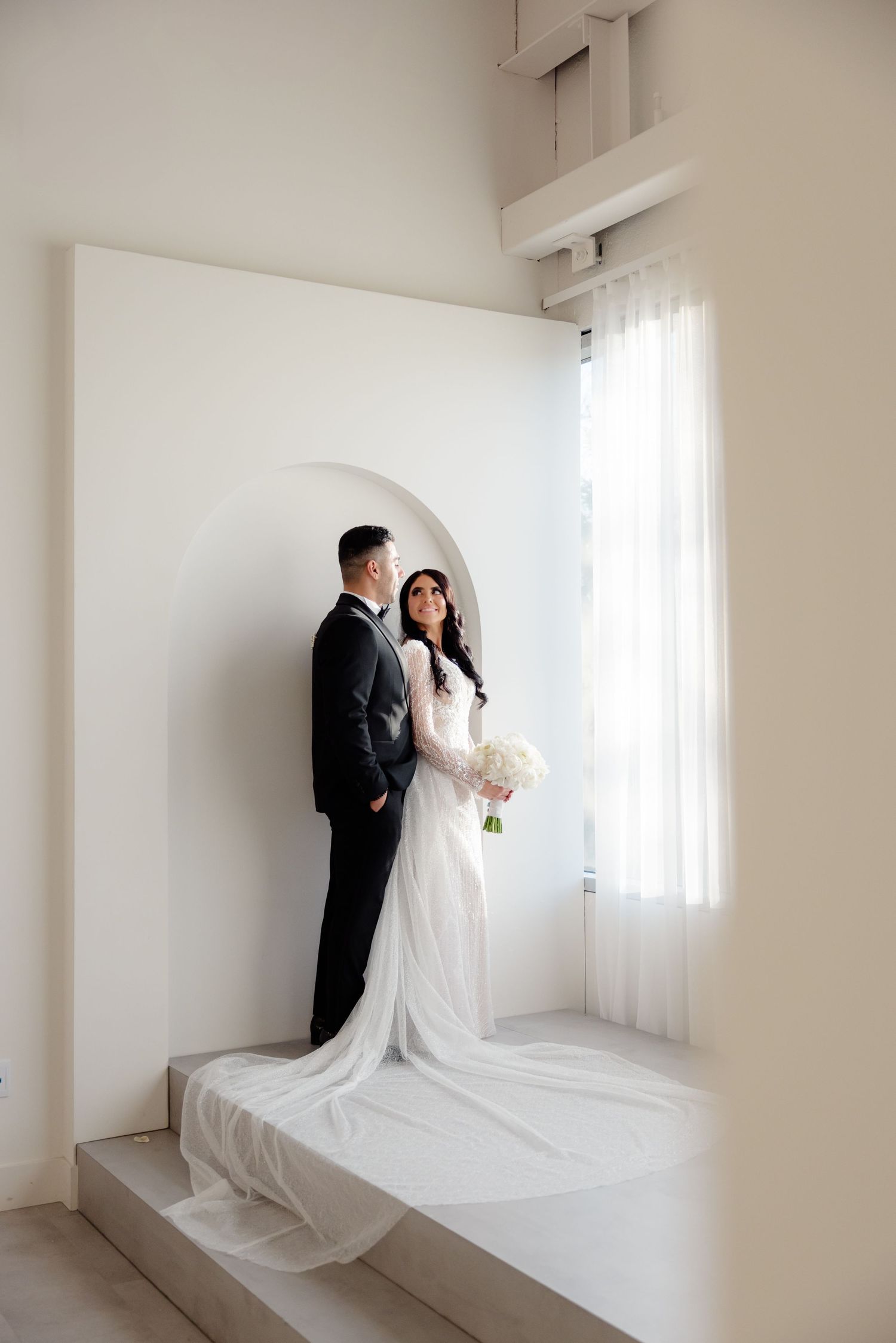 Artistic wedding portrait showing couple framed within curved white archway.