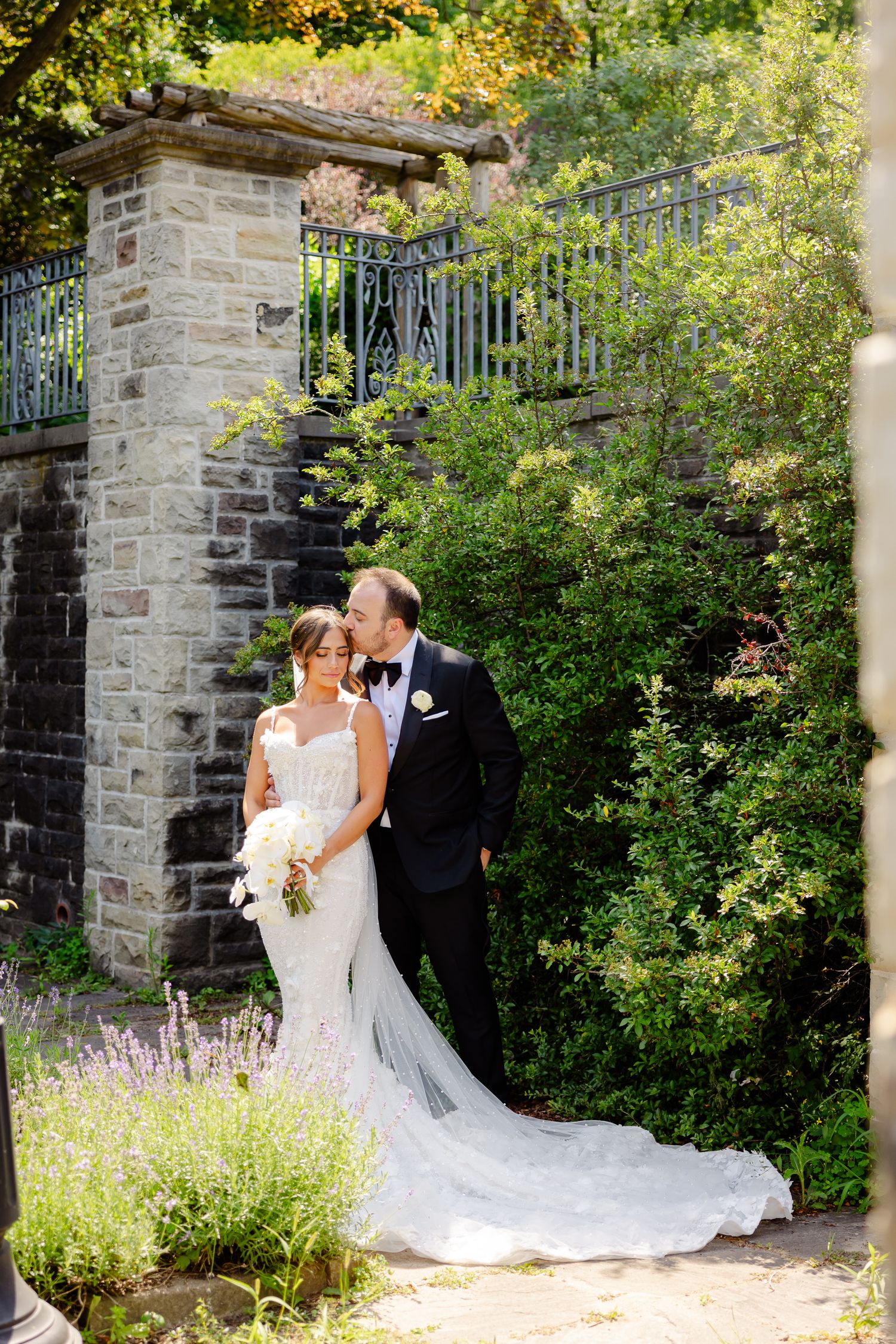 Romantic wedding scene under a stone archway with lush greenery and lavender blooms in the garden.