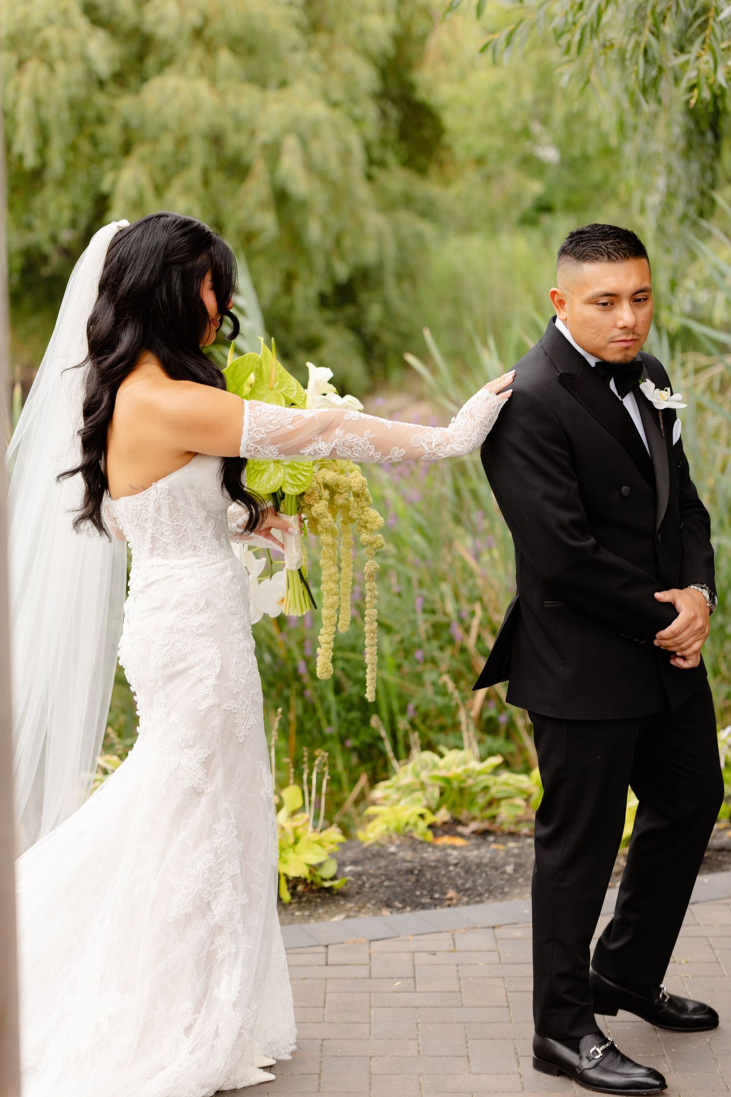 Newlyweds share a playful dance moment on a stone patio with lush greenery in the background.