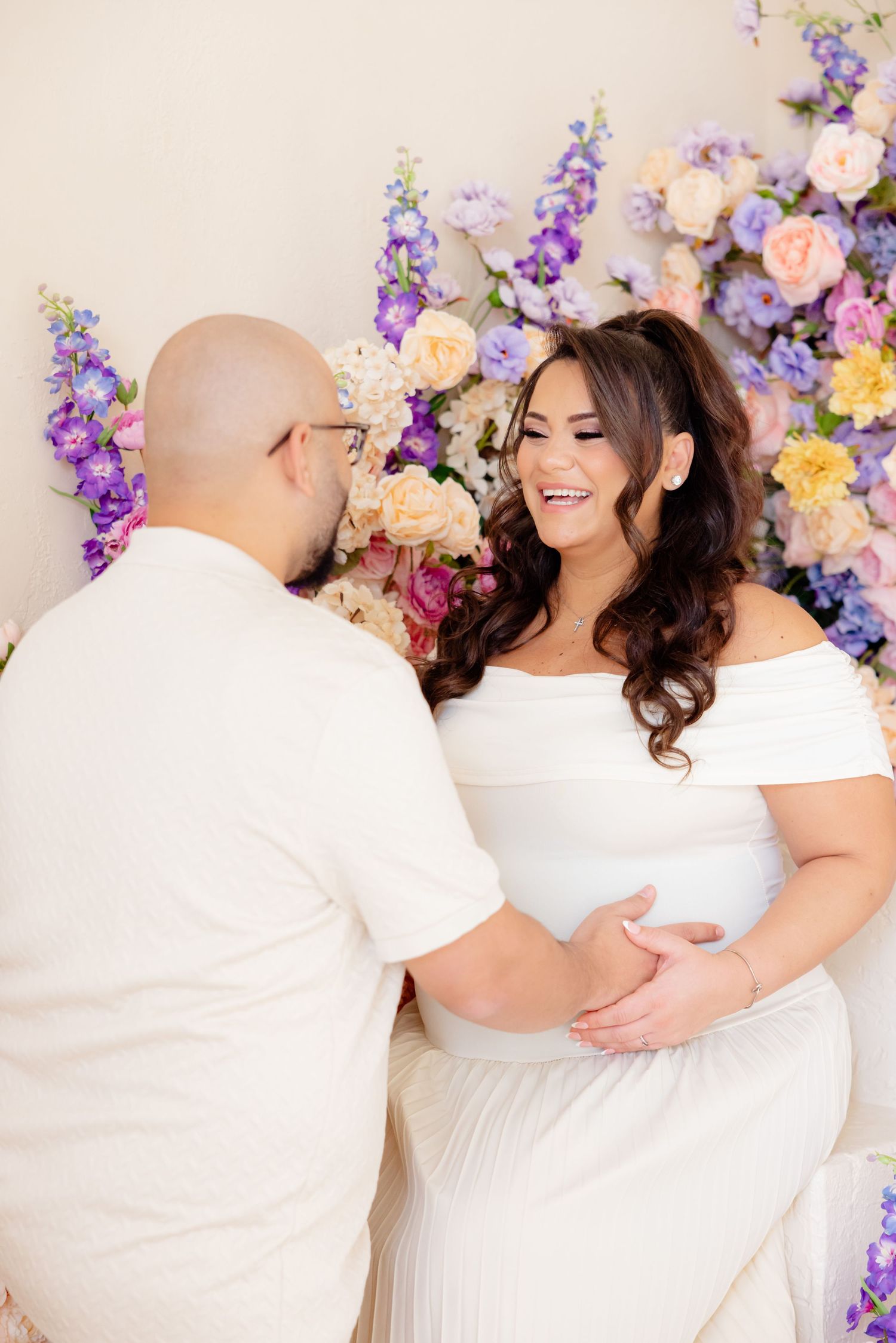 A couple shares an intimate moment against a backdrop of pink, purple and white floral decorations.