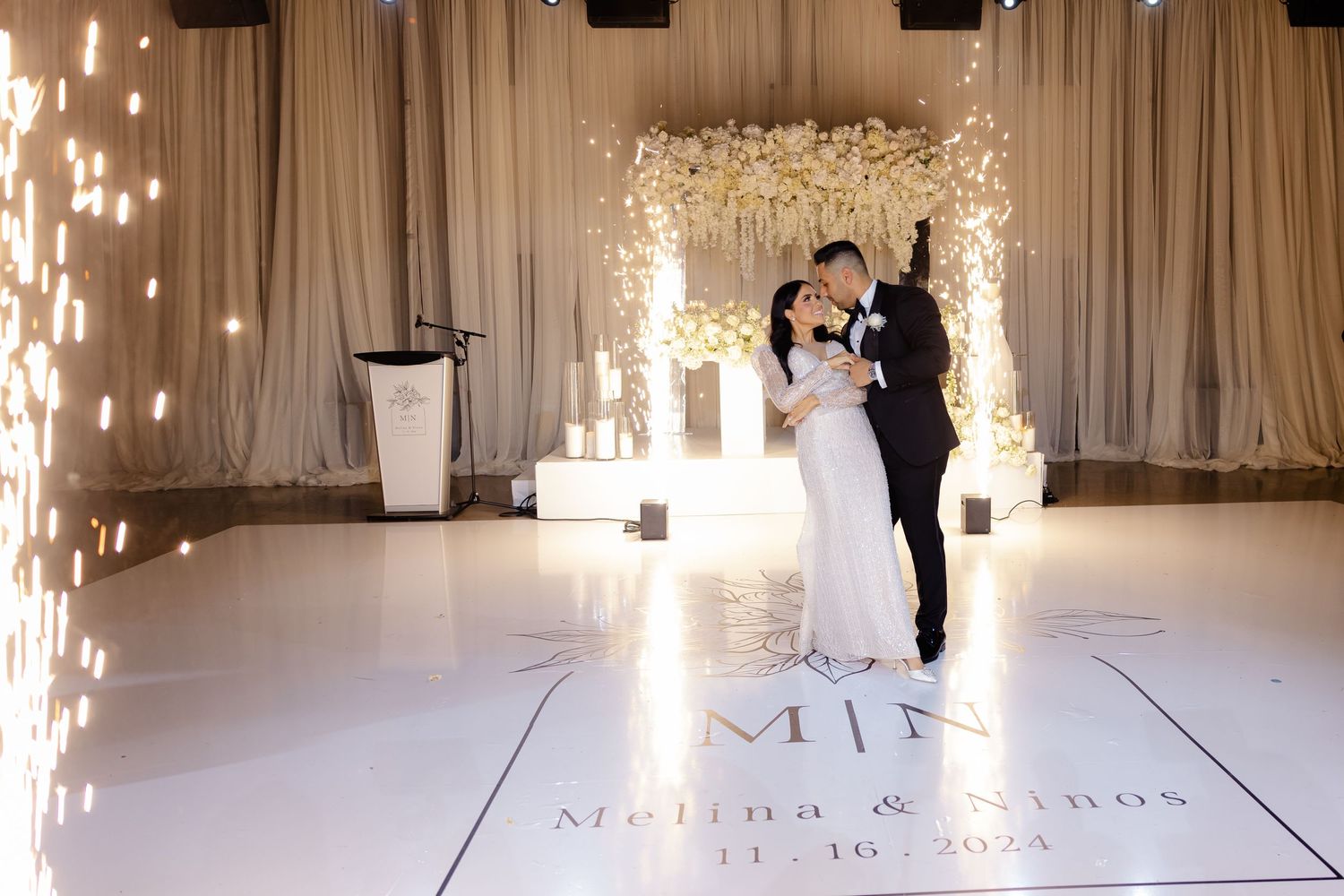 Romantic wedding dance under floral arch with sparkler effects and custom monogrammed dance floor.