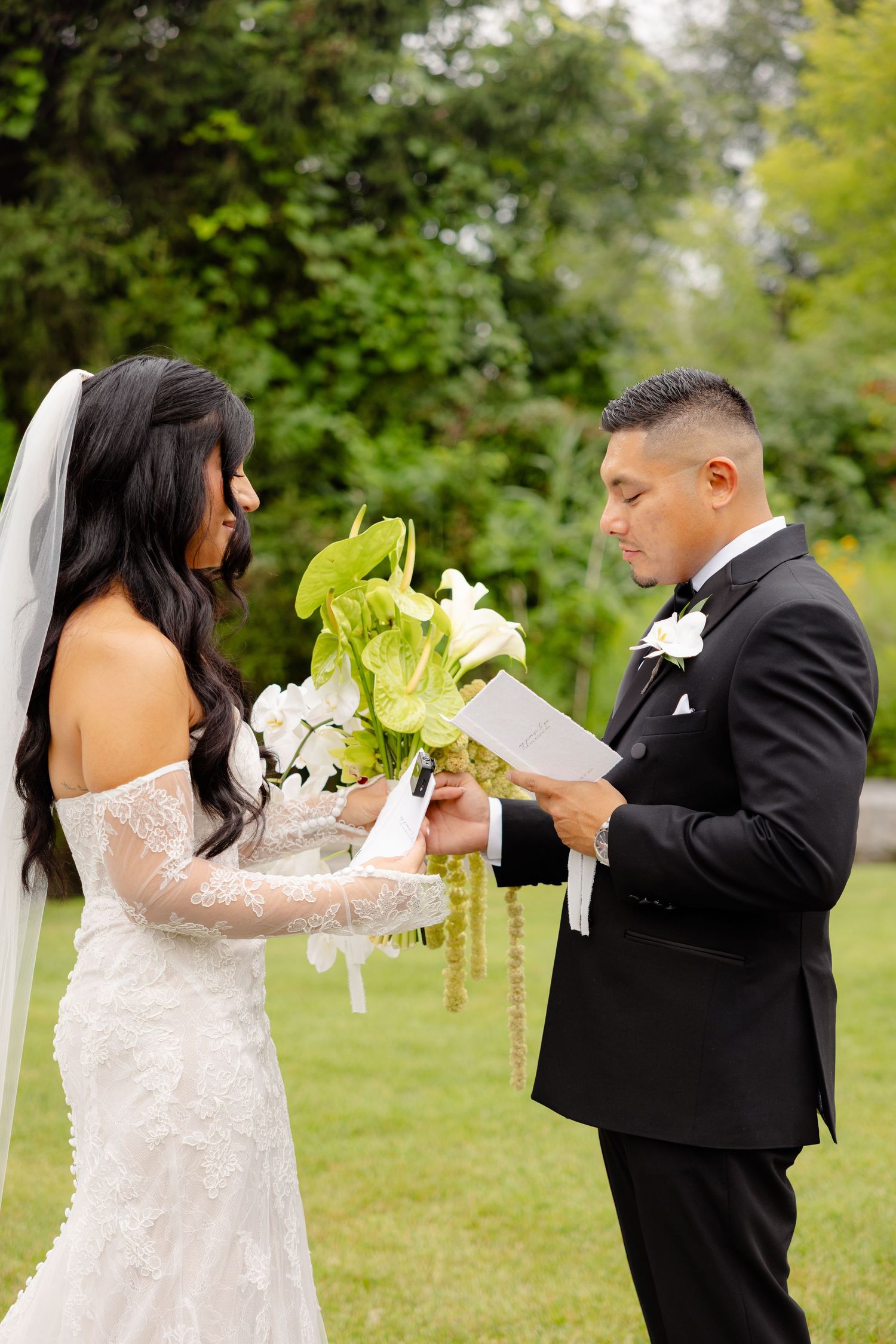 A newlywed couple shares a playful moment with their wedding bouquet in an outdoor garden setting.