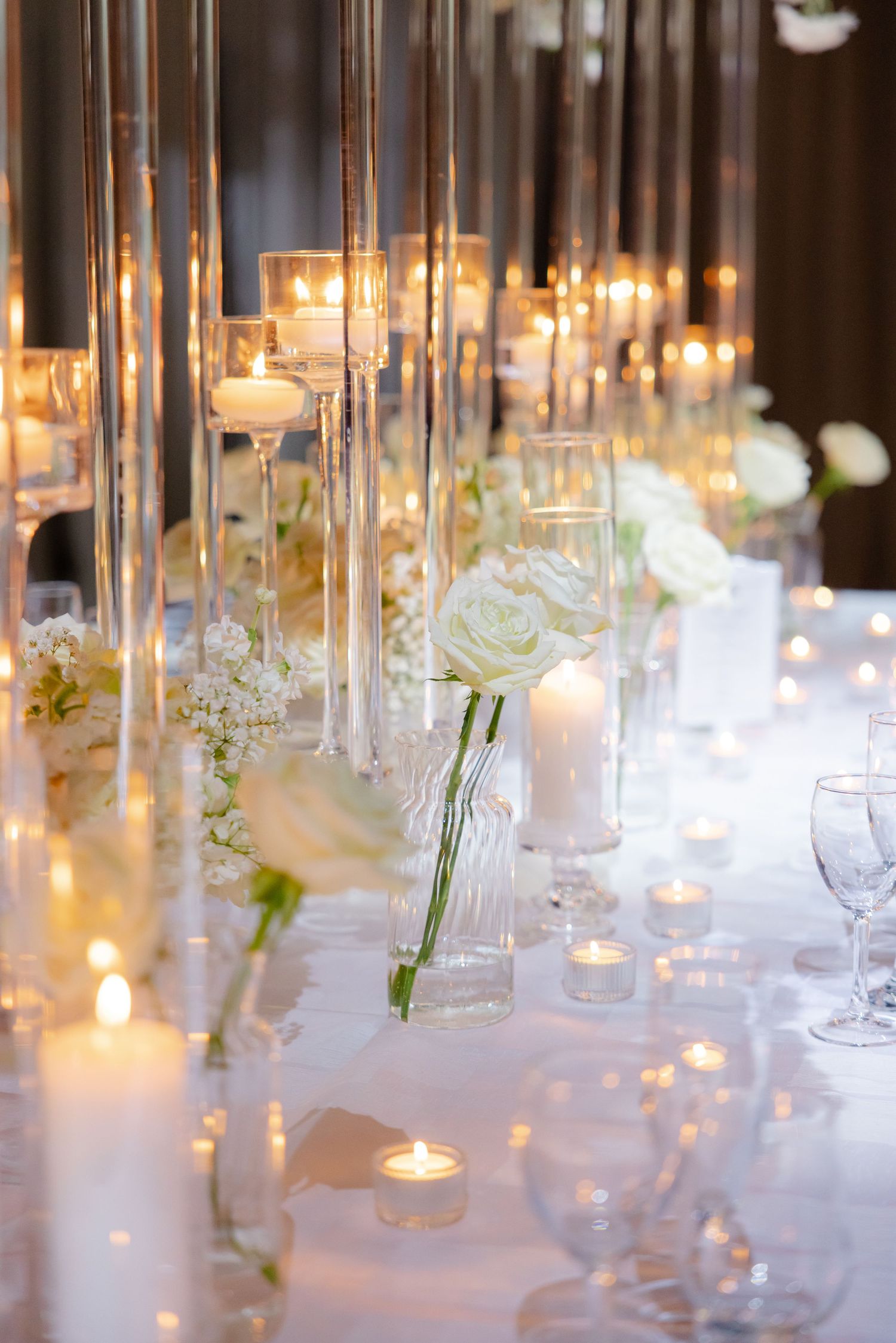 Close-up of romantic table setting with glass candlesticks and white roses creating an ethereal atmosphere.