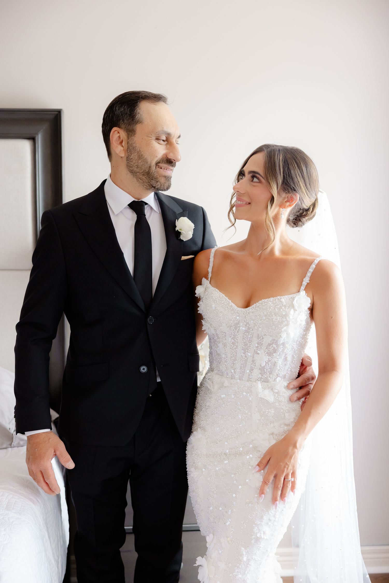 Happy bride and groom share tender moment together, she wears lace gown with veil and he wears classic black suit.