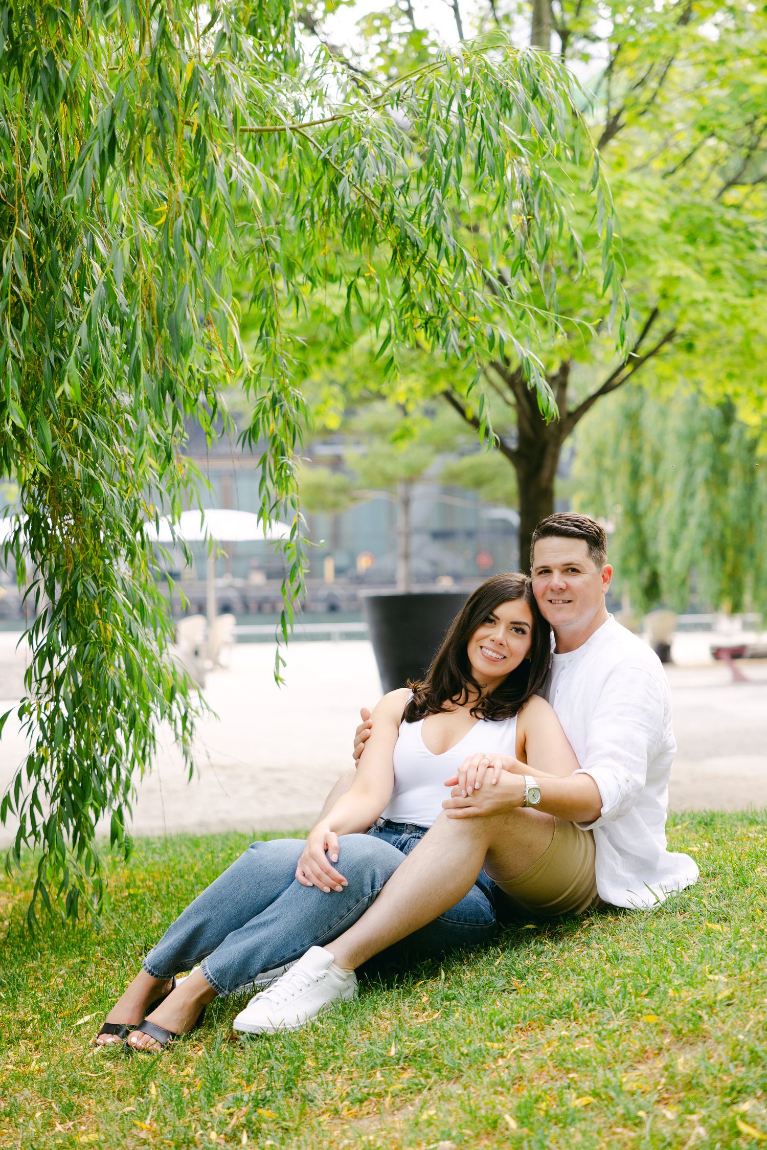 Romantic couple lounging on grass beneath weeping willow branches.