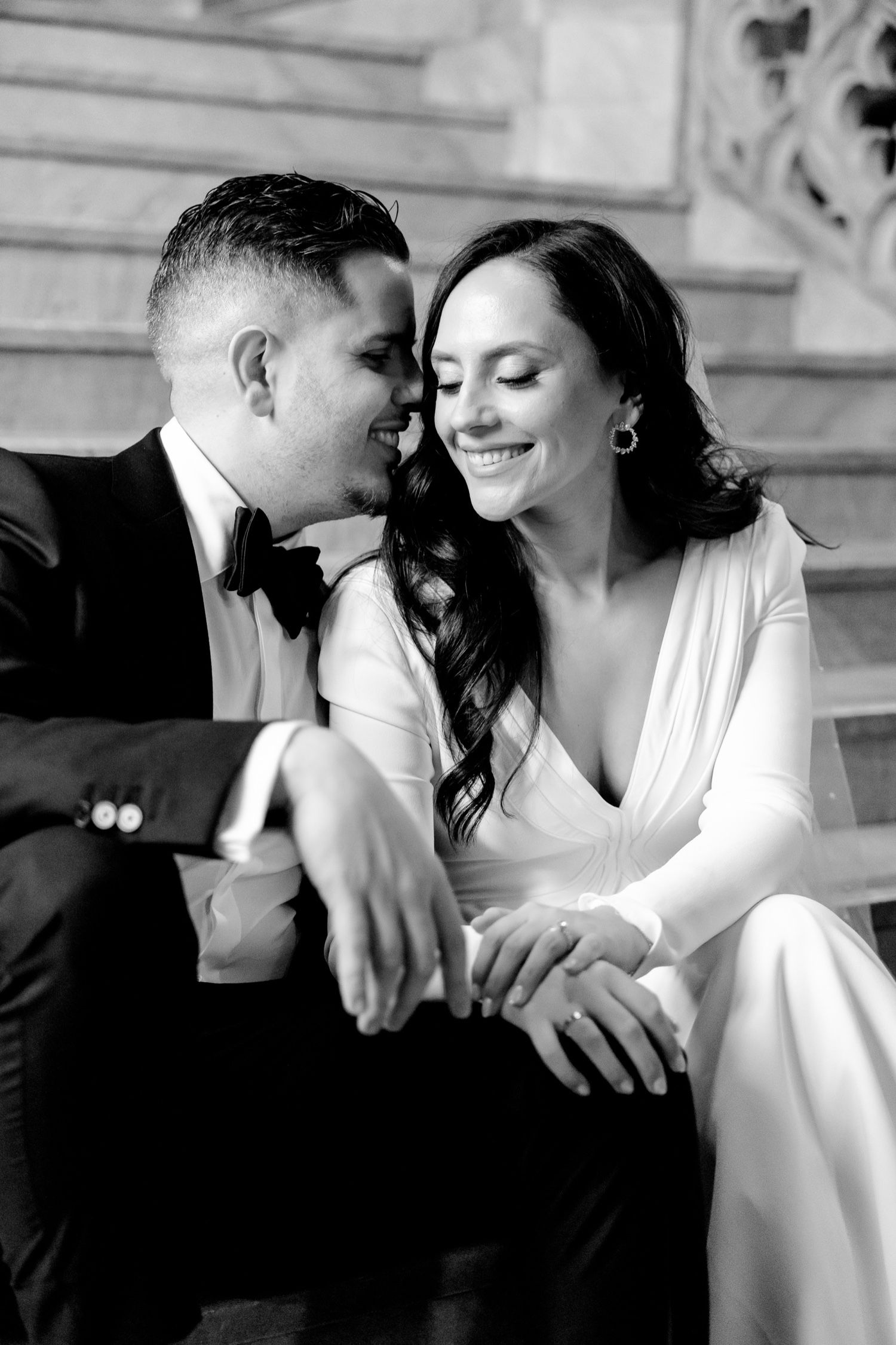 A romantic black and white wedding portrait shows a couple sharing an intimate moment on stone steps.