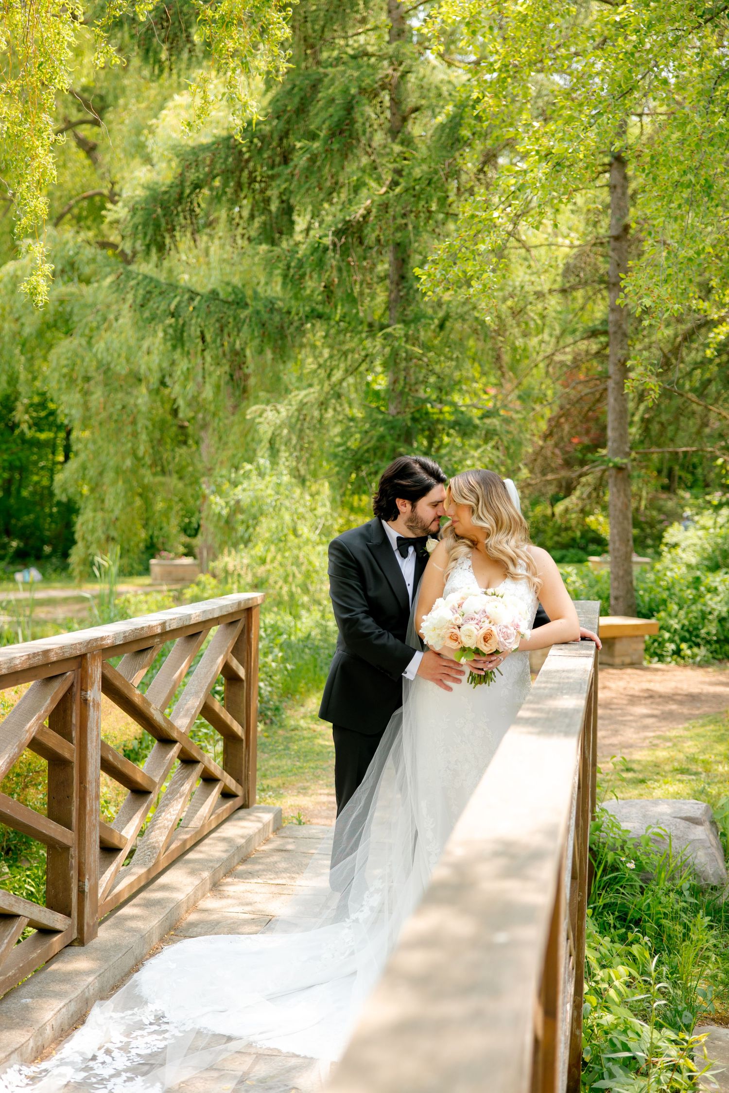 Dreamy wedding portrait on wooden bridge with cascading veil and garden backdrop.