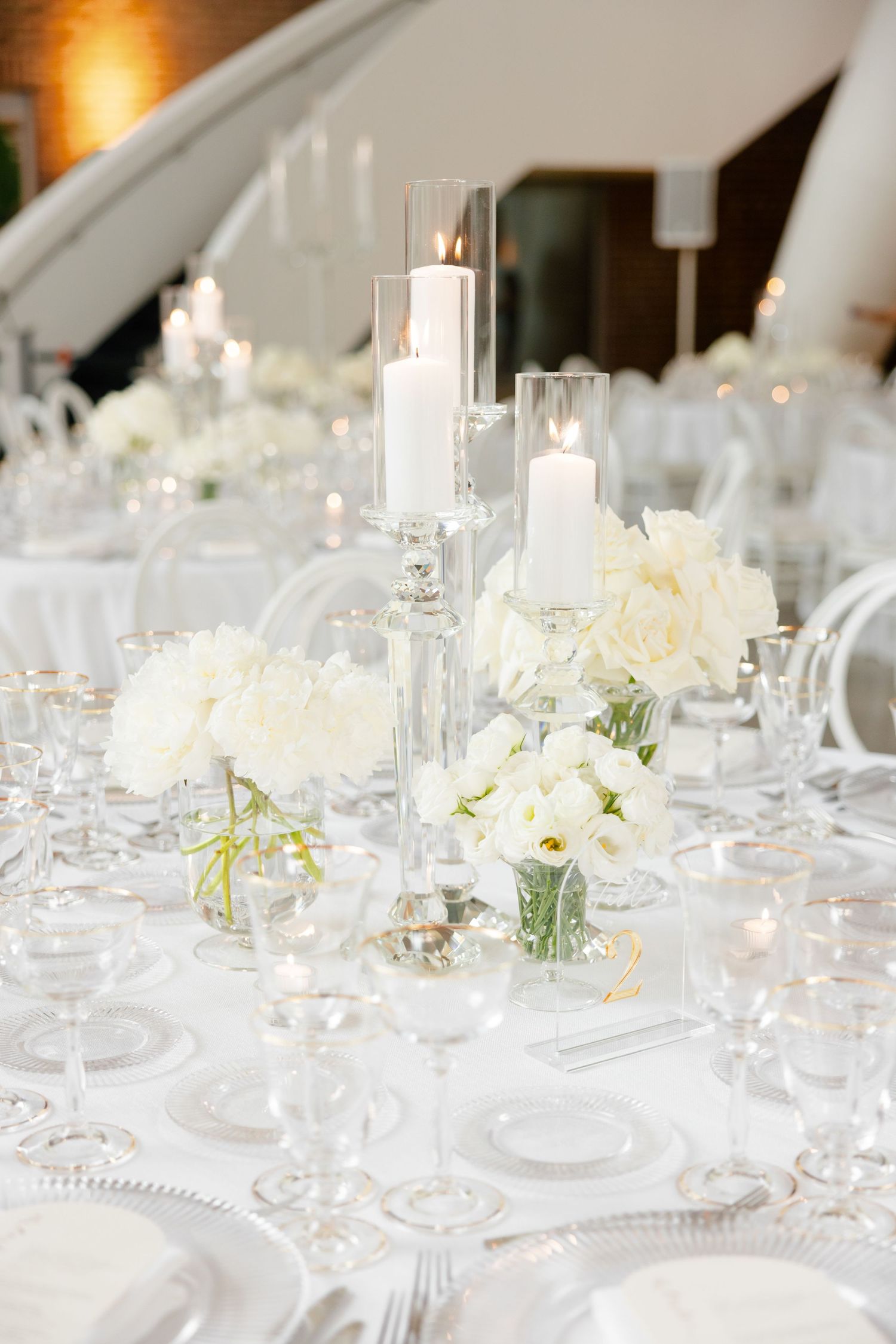 White floral centerpieces and candles on elegant wedding reception table with crystal glassware.