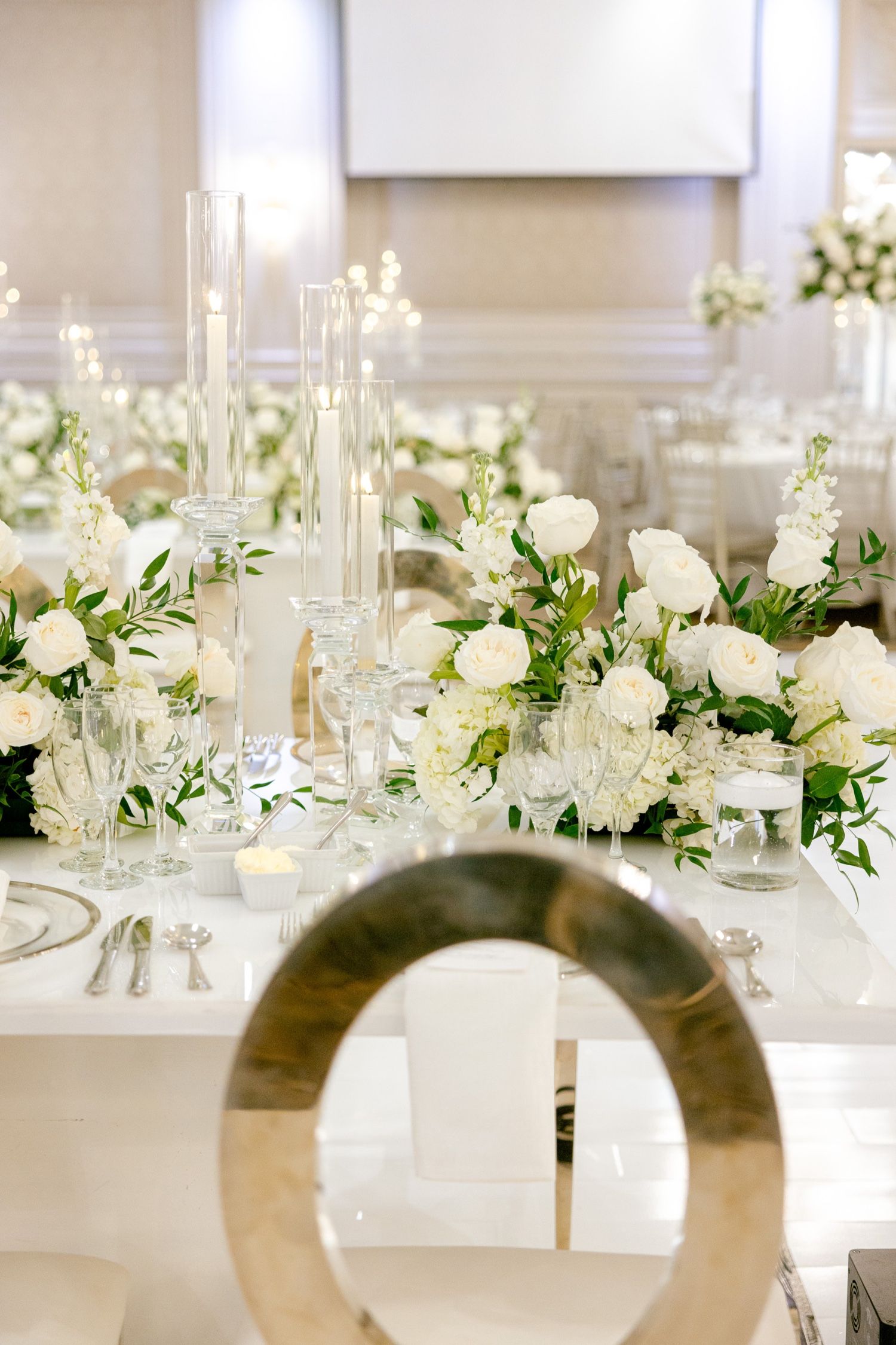 Luxurious wedding table setting with white roses, crystal glassware, and gold accents.