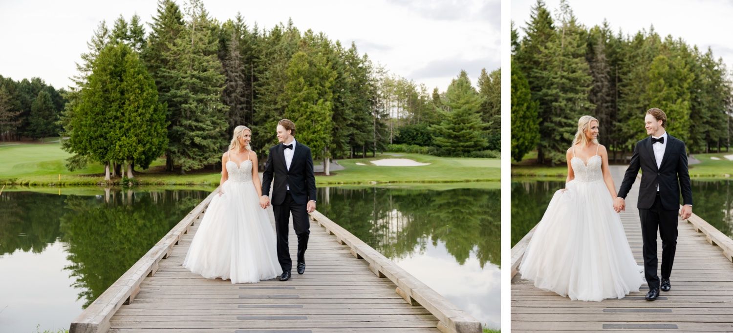 Couple walking together on wooden bridge surrounded by evergreen trees and pond.