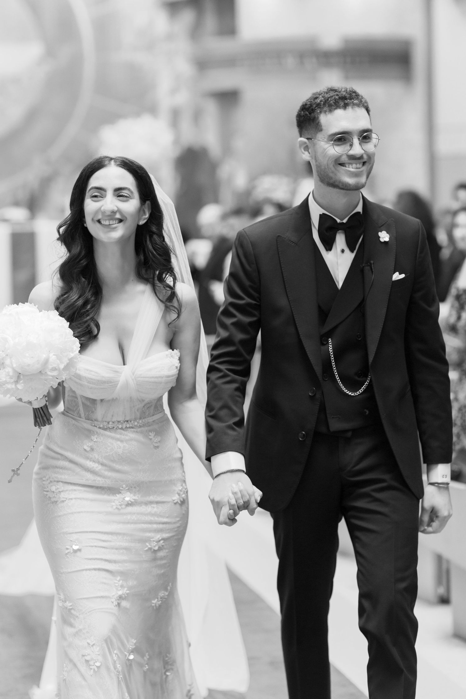 A black and white photo of a couple walking together on their wedding day.