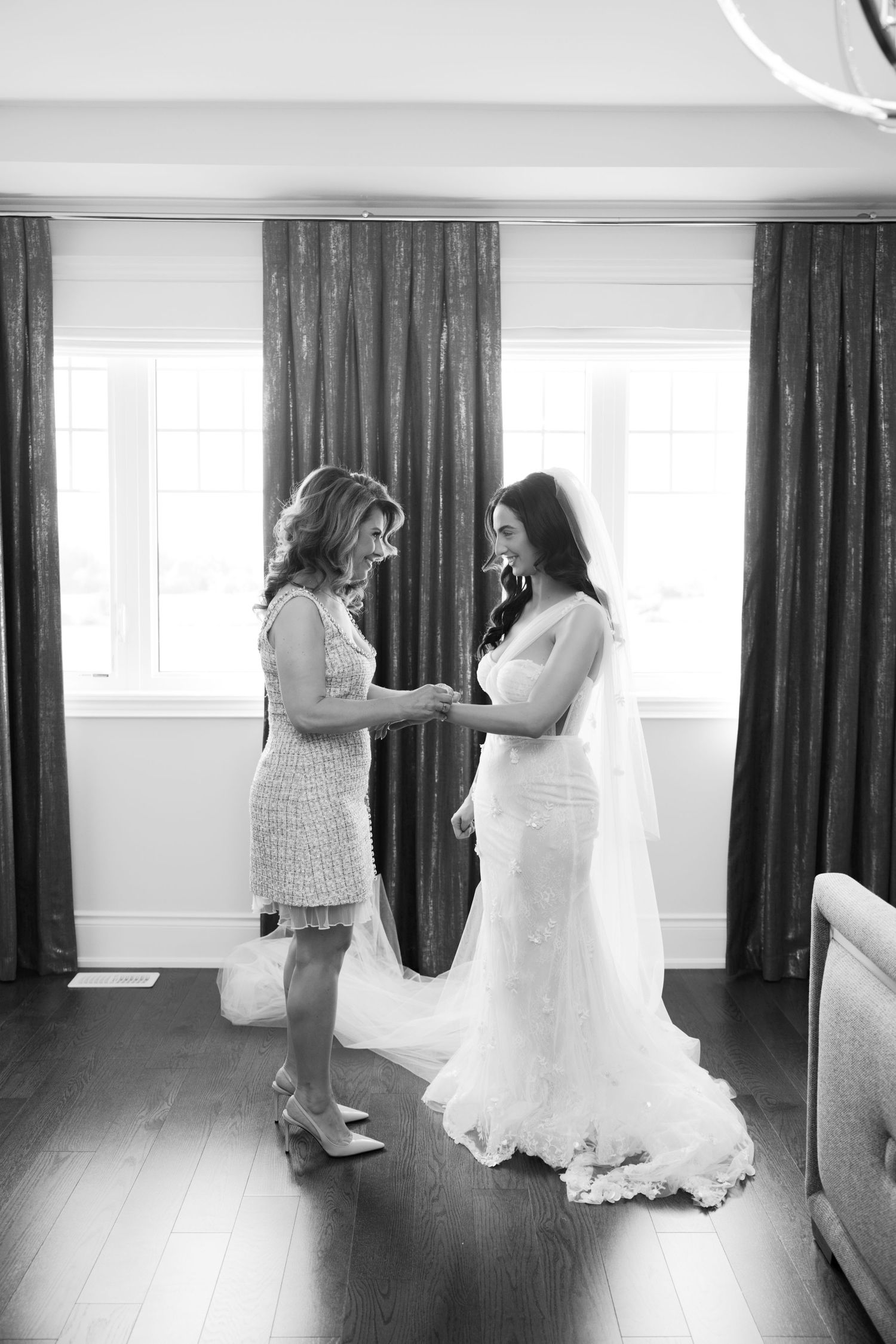 A touching bridal preparation moment in a room with elegant dark curtains and hardwood floors.