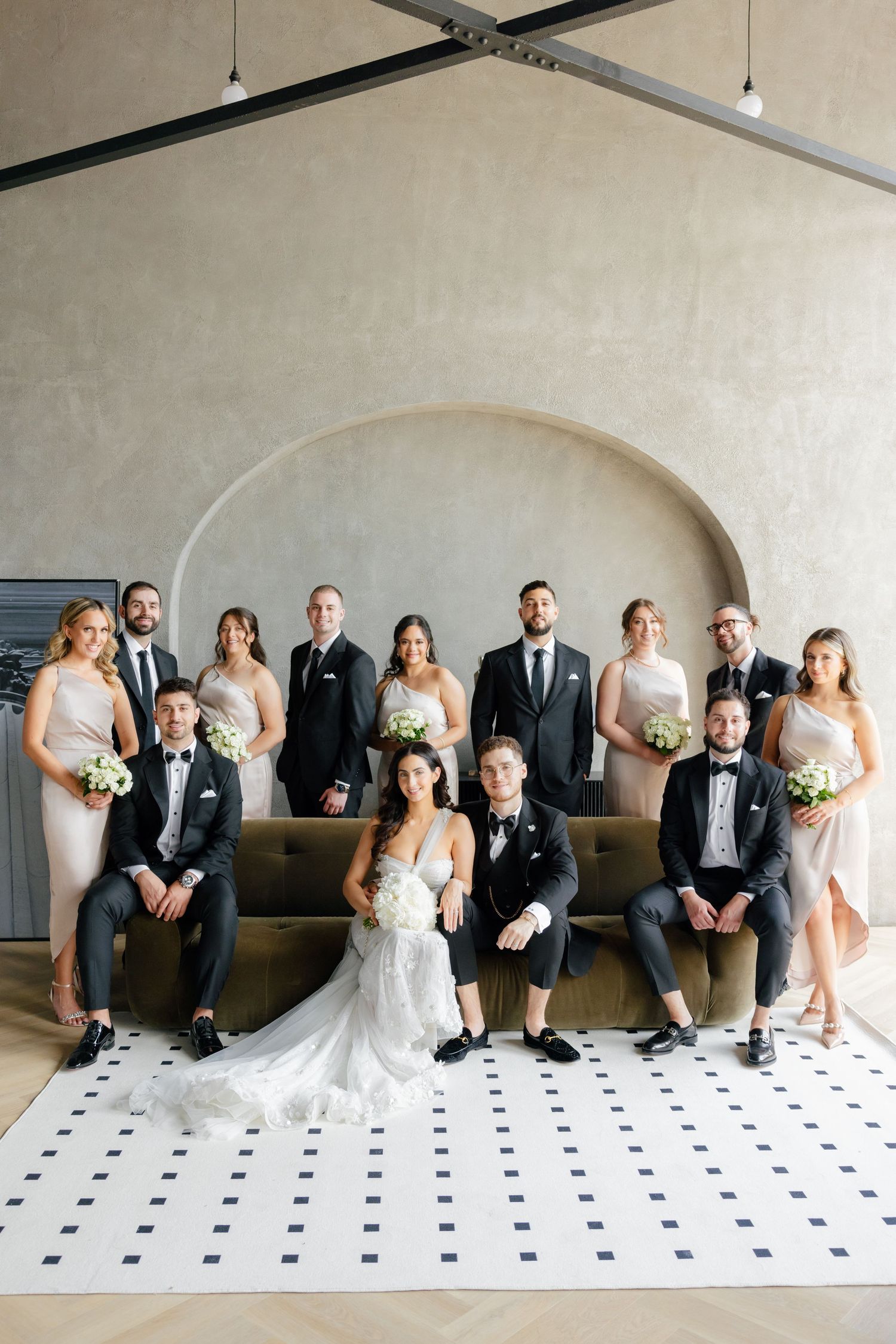 Full wedding party portrait with bridesmaids in light dresses and groomsmen in dark suits.