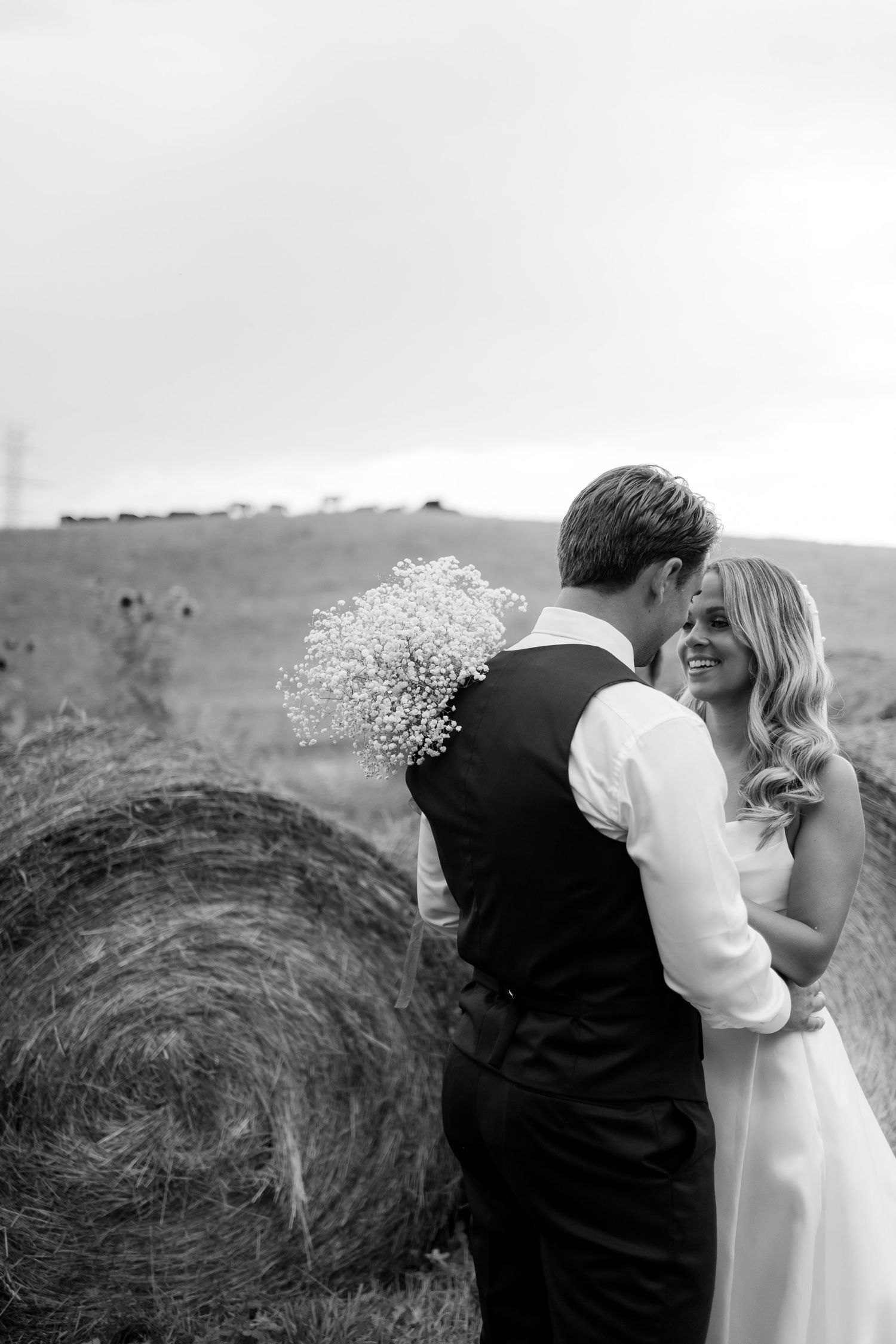 A black and white wedding portrait showing a tender moment between the couple near hay bales.