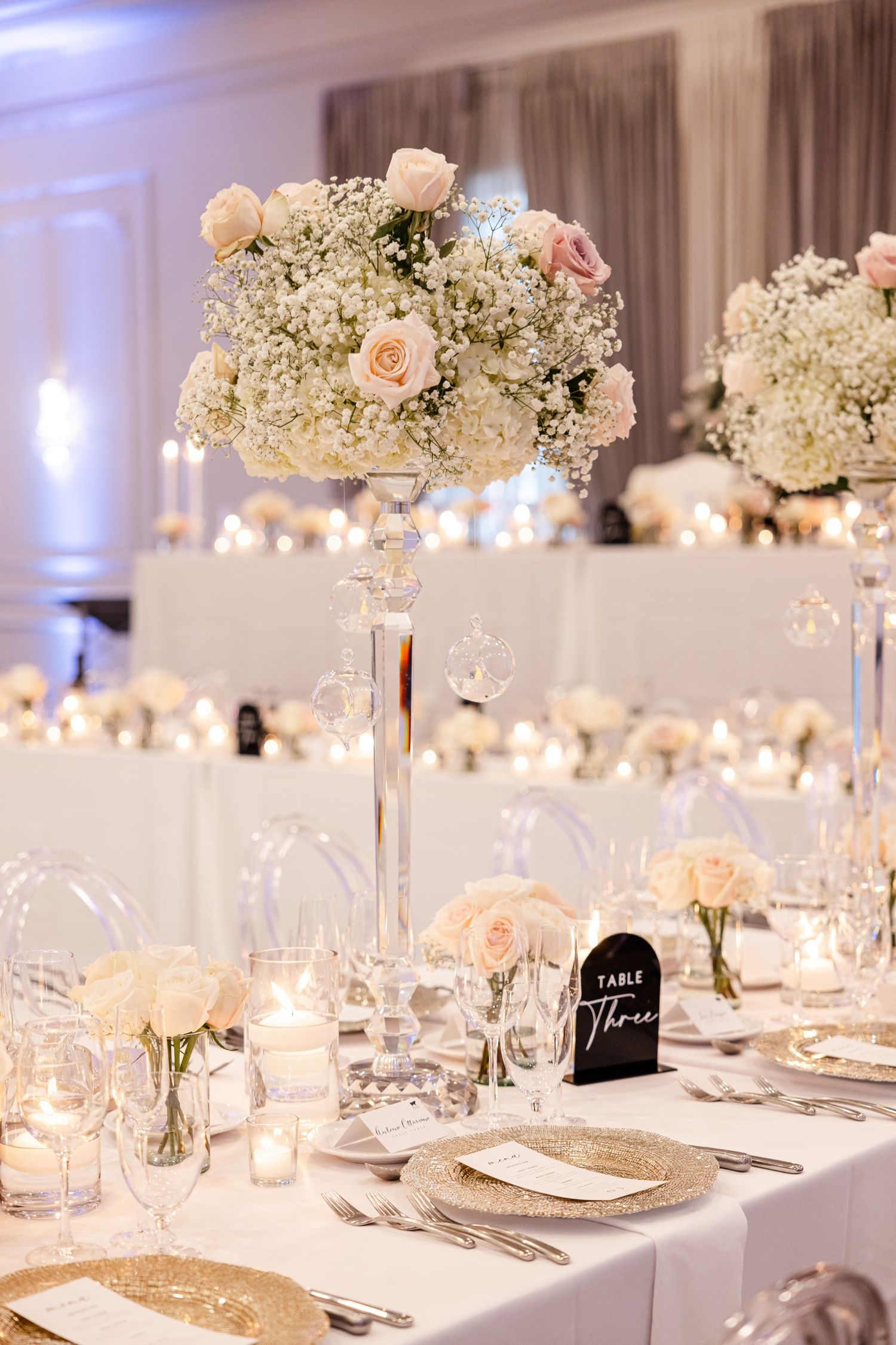 Luxurious table decor featuring tall white and blush floral arrangements with baby's breath on crystal stands.