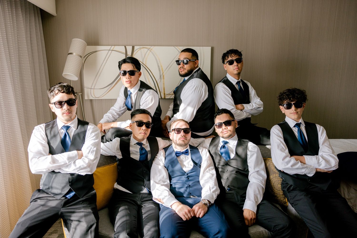 Group of groomsmen wearing sunglasses pose confidently in matching formal wear.