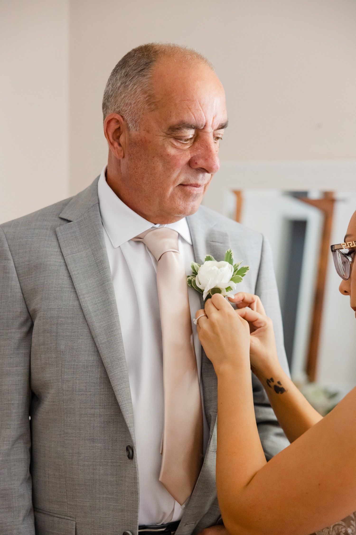 A touching moment as someone pins a white boutonniere on a gray suit.