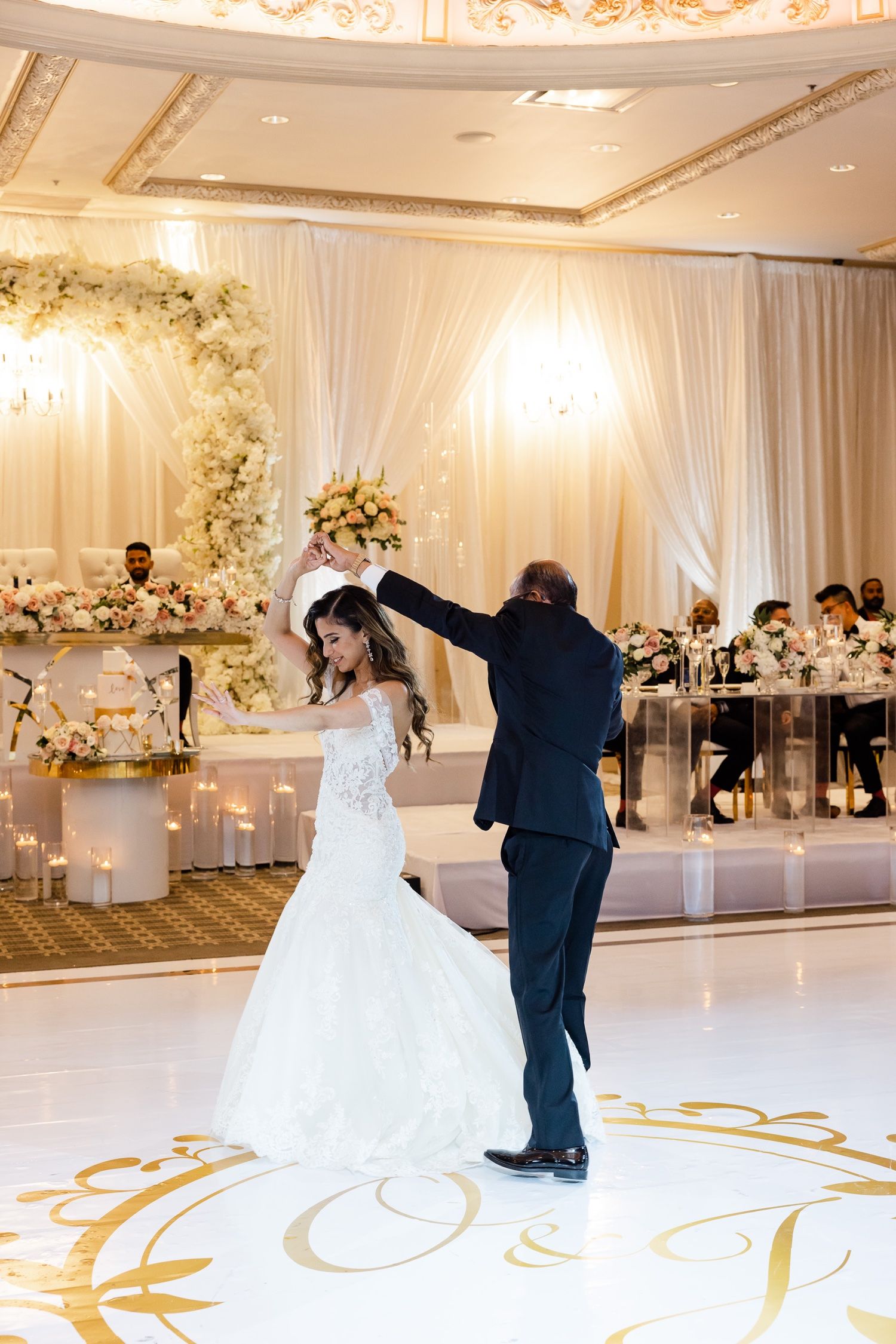 Wedding couple twirls on a decorated dance floor with floral arch and elegant white draping in the background.