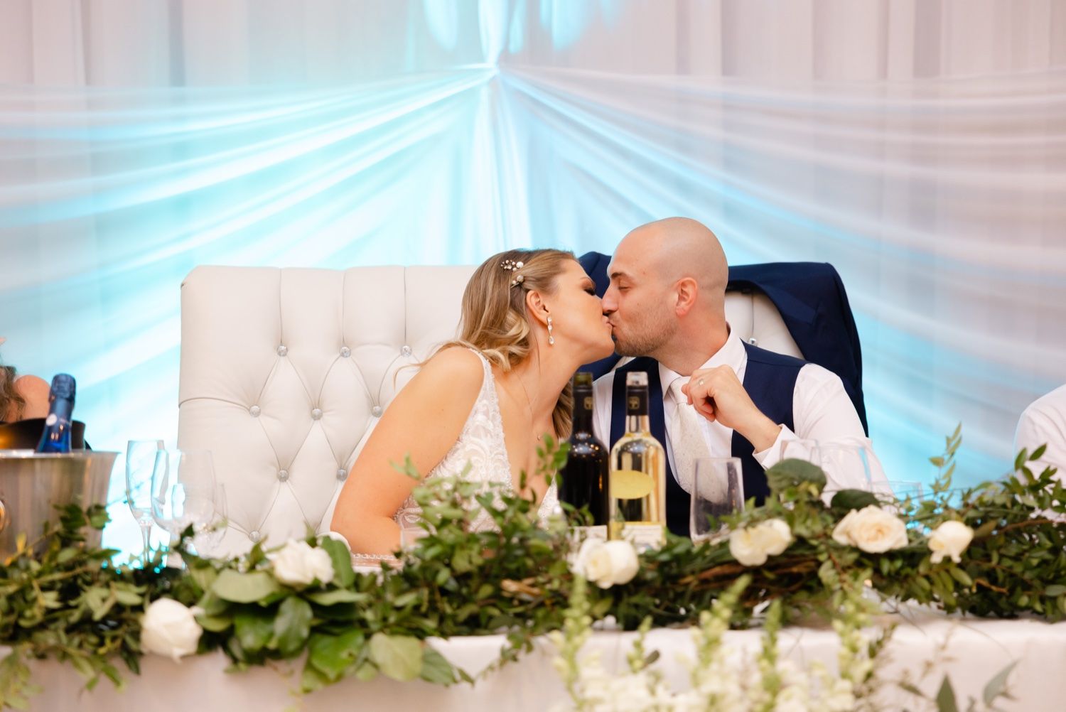 Romantic moment between couple at wedding reception head table with floral decor.