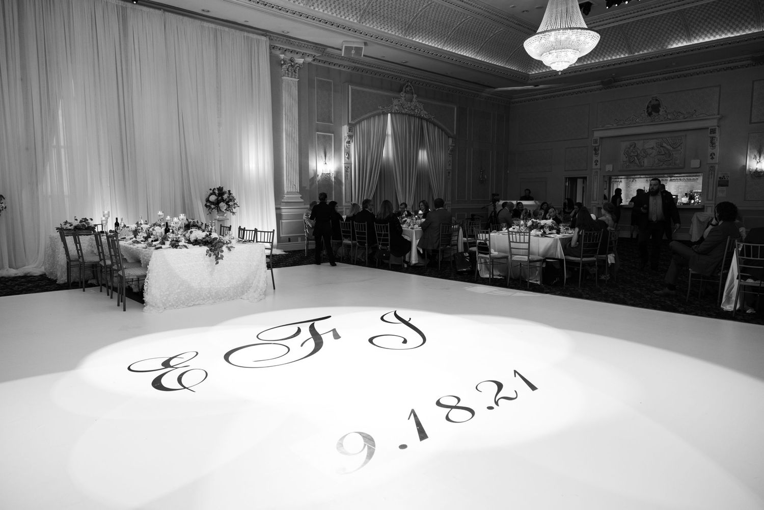 Elegant ballroom reception setup with monogrammed dance floor and white draping.