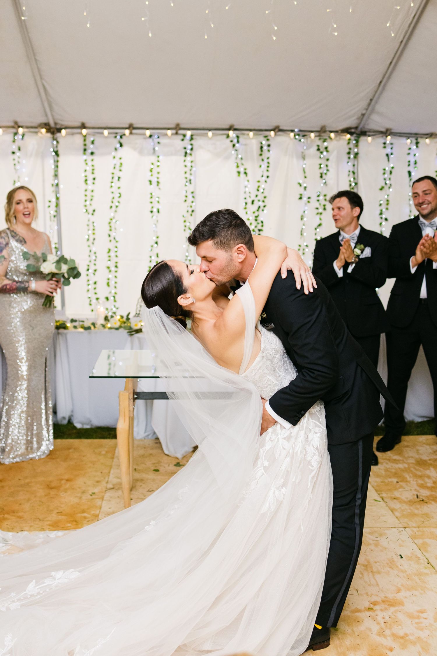 Romantic dip during first dance with sparkly-dressed guest and wedding party watching.