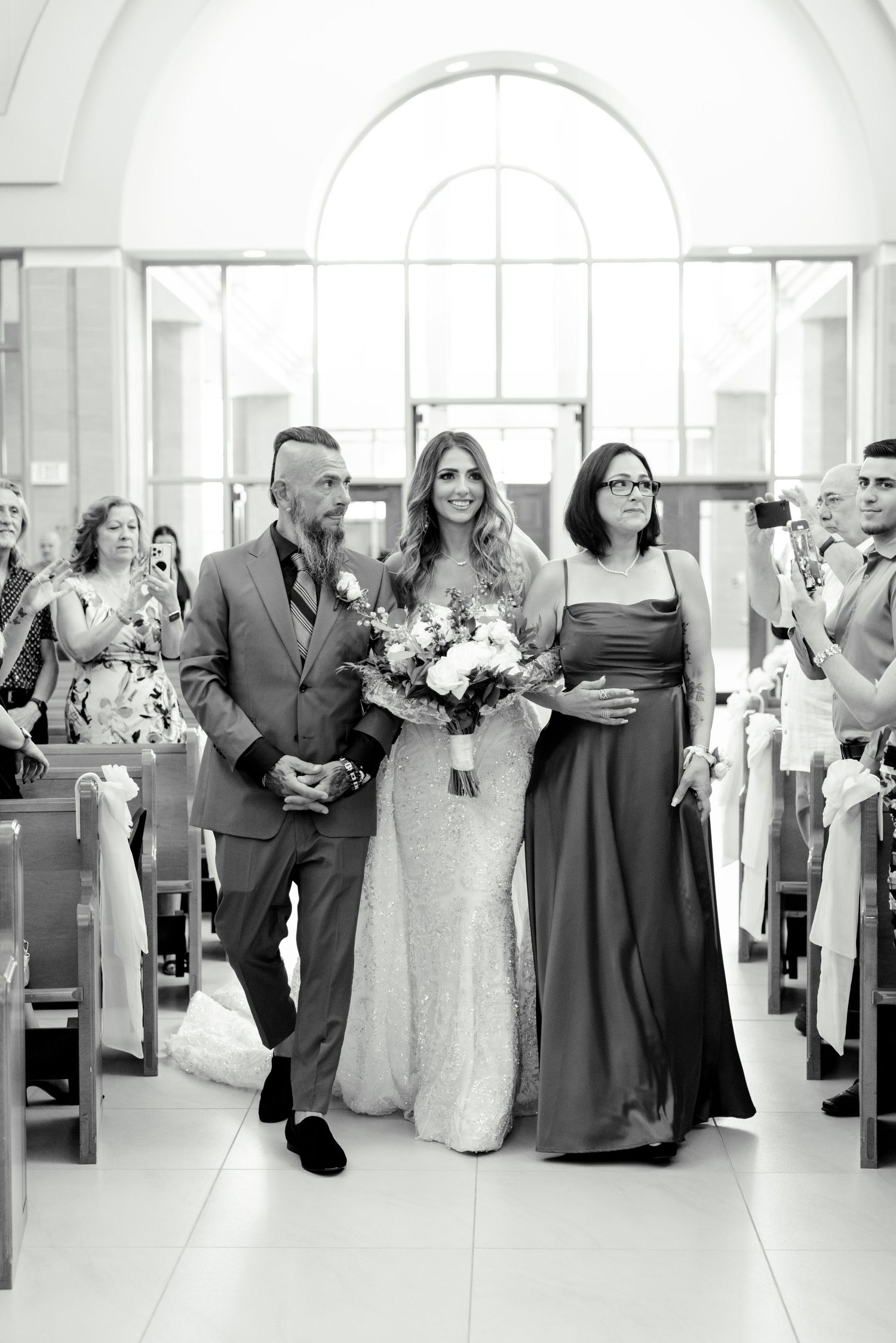 A black and white photo of a wedding processional with guests applauding in church pews.