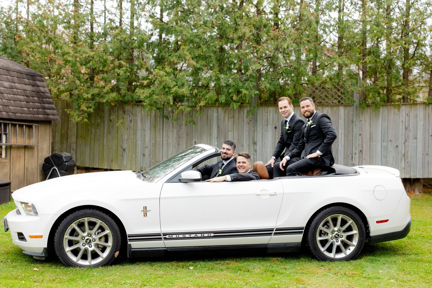 A group poses with a white convertible Mustang on a grass lawn.