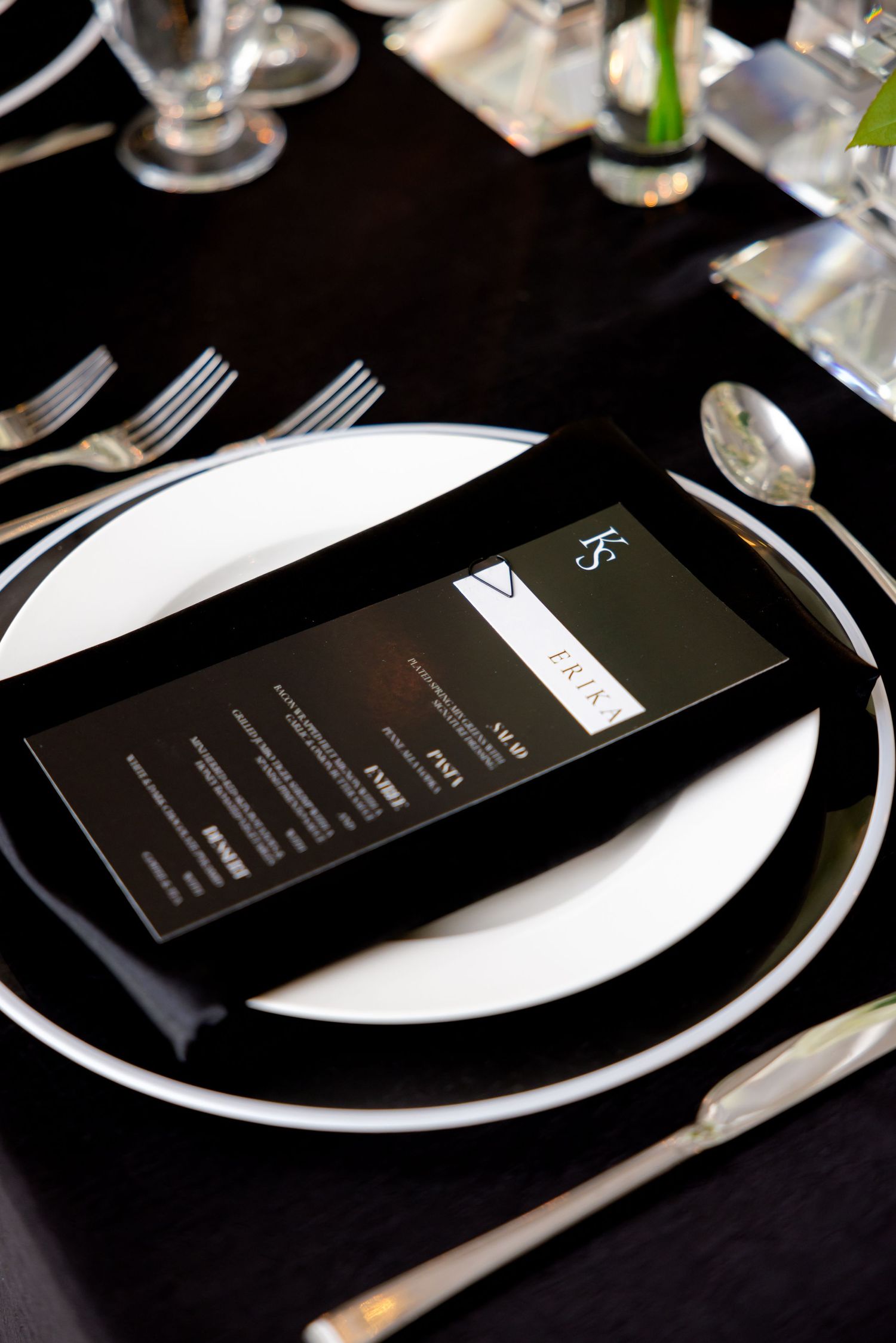 Modern black menu card on white plate with elegant place setting at wedding reception.